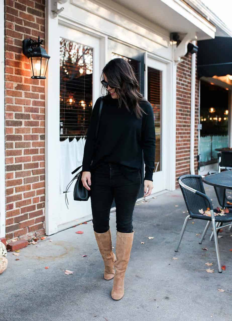 Black turtleneck and black jeans with brown tall boots and black bag standing outside a cafe.
