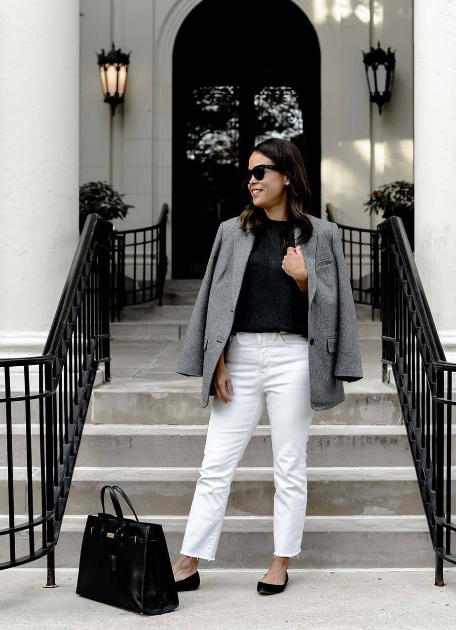 standing with grey blazer and white jeans in front of a building