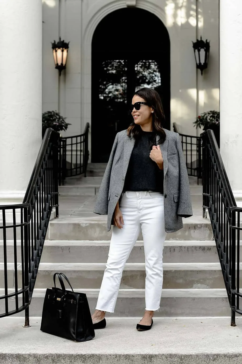 standing with grey blazer and white jeans in front of a building