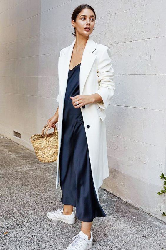 woman wearing navy dress with white sneakers and white coat 