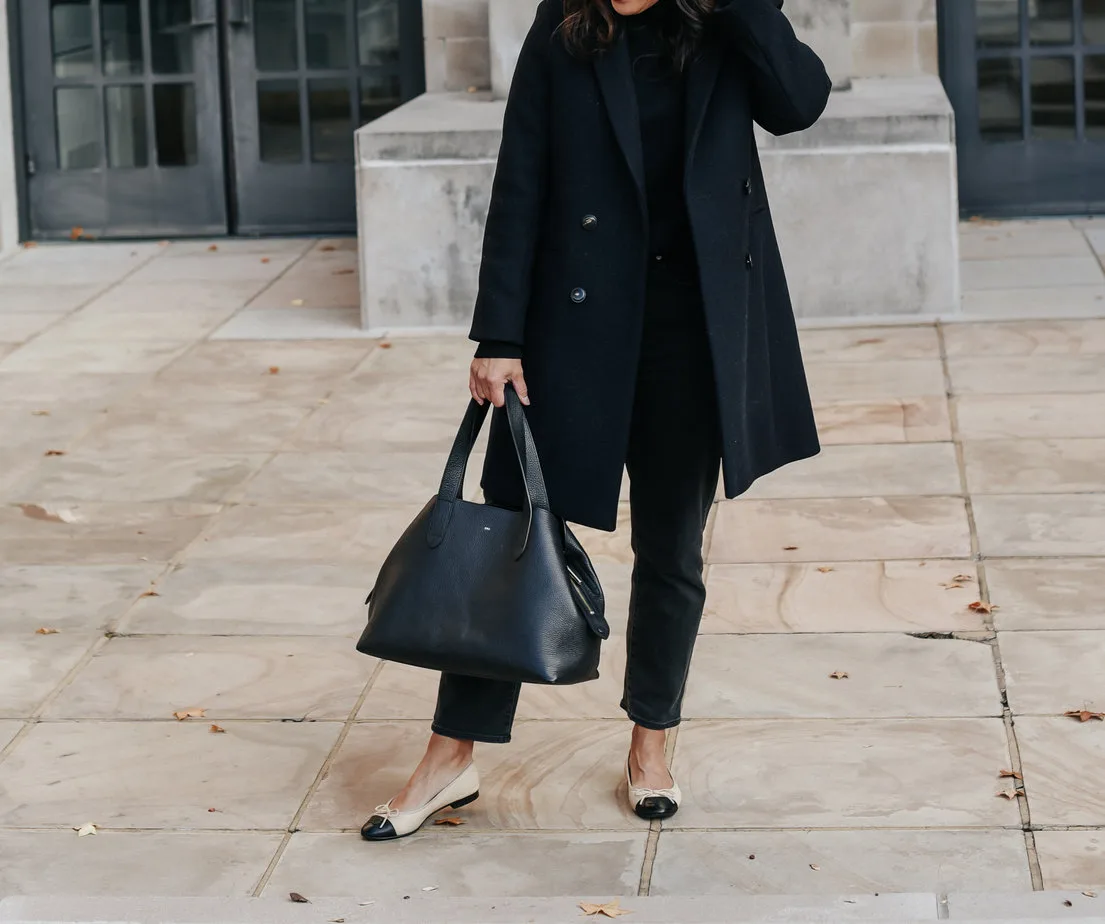 Lady wearing dark navy coat with ballet flats, black handbag, black denim