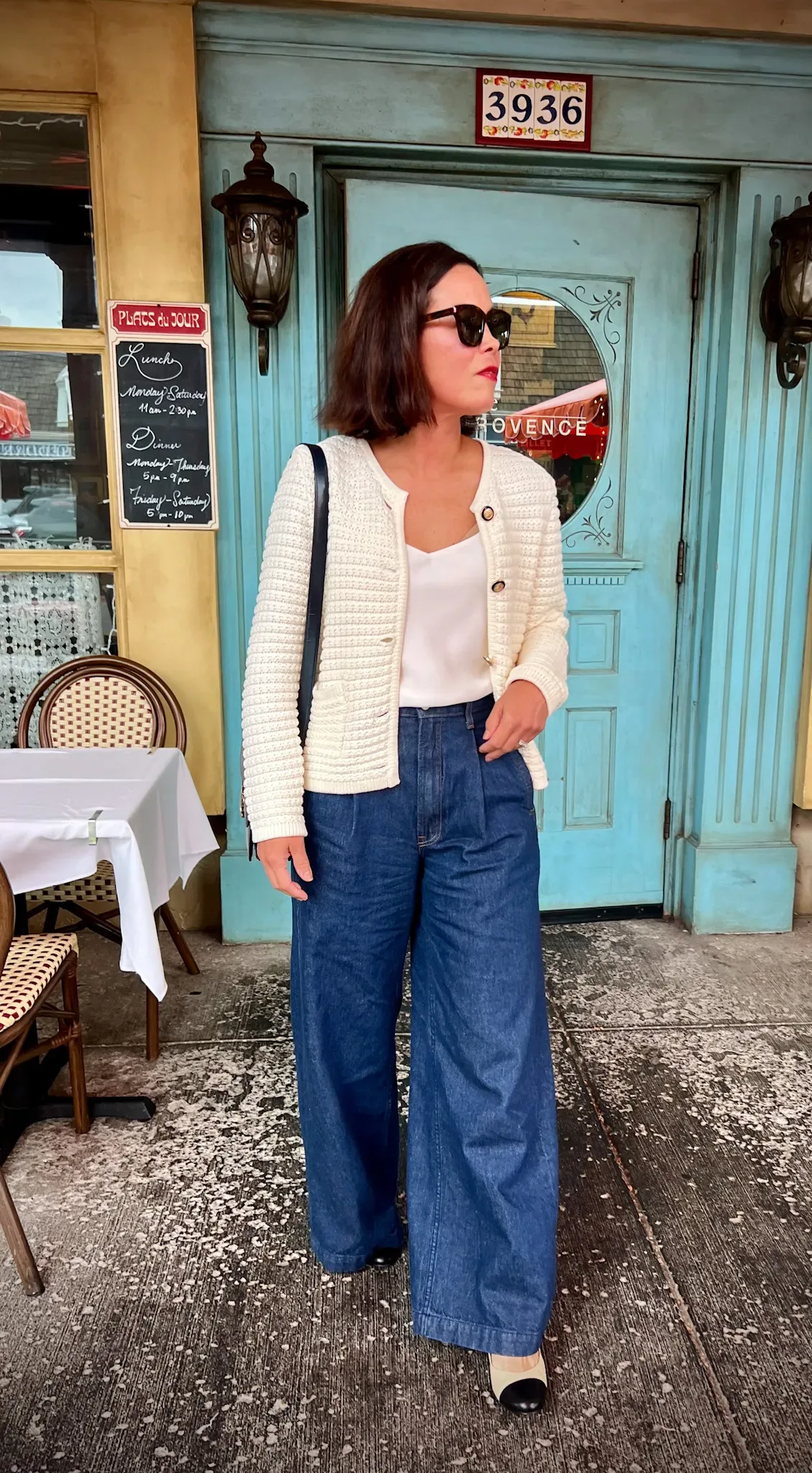 Woman wearing cream cardigan and jeans walking out of a door.