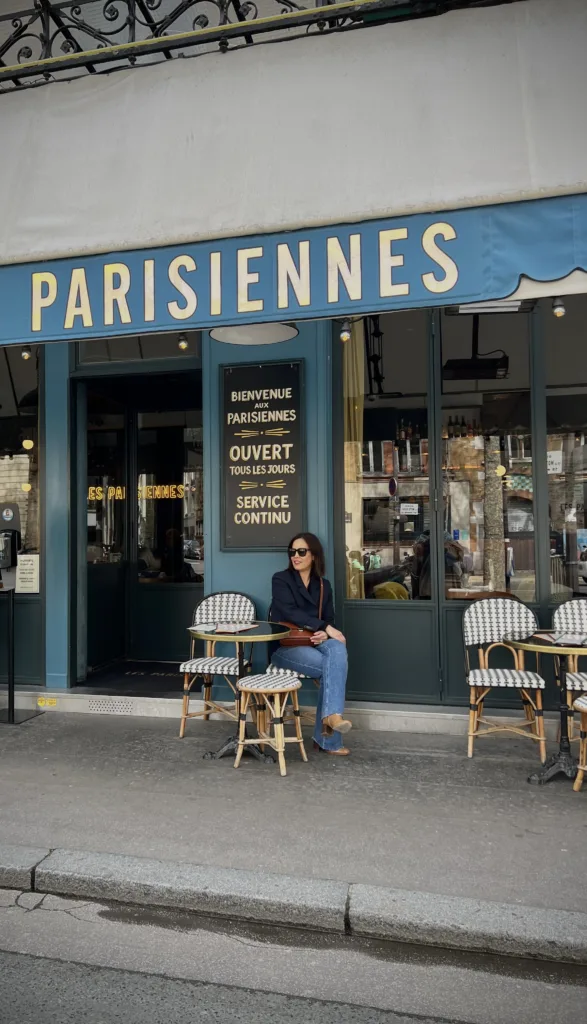 Woman wearing navy blazer with jeans sitting at a cafe. Jean outfits to wear in Paris.