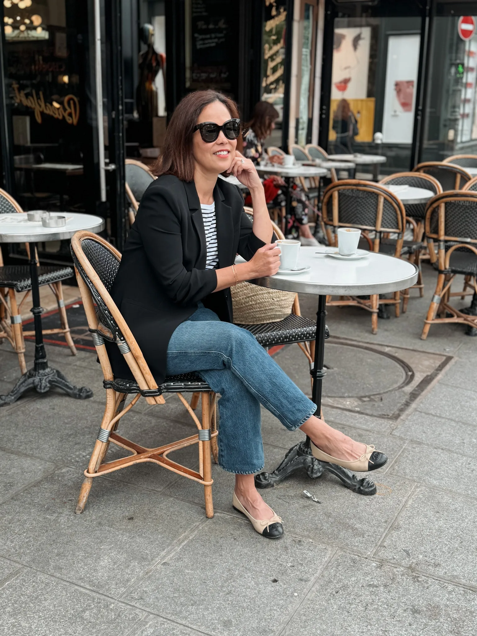 Woman sitting at a cafe wearing black blazer and ballet flats in Paris.