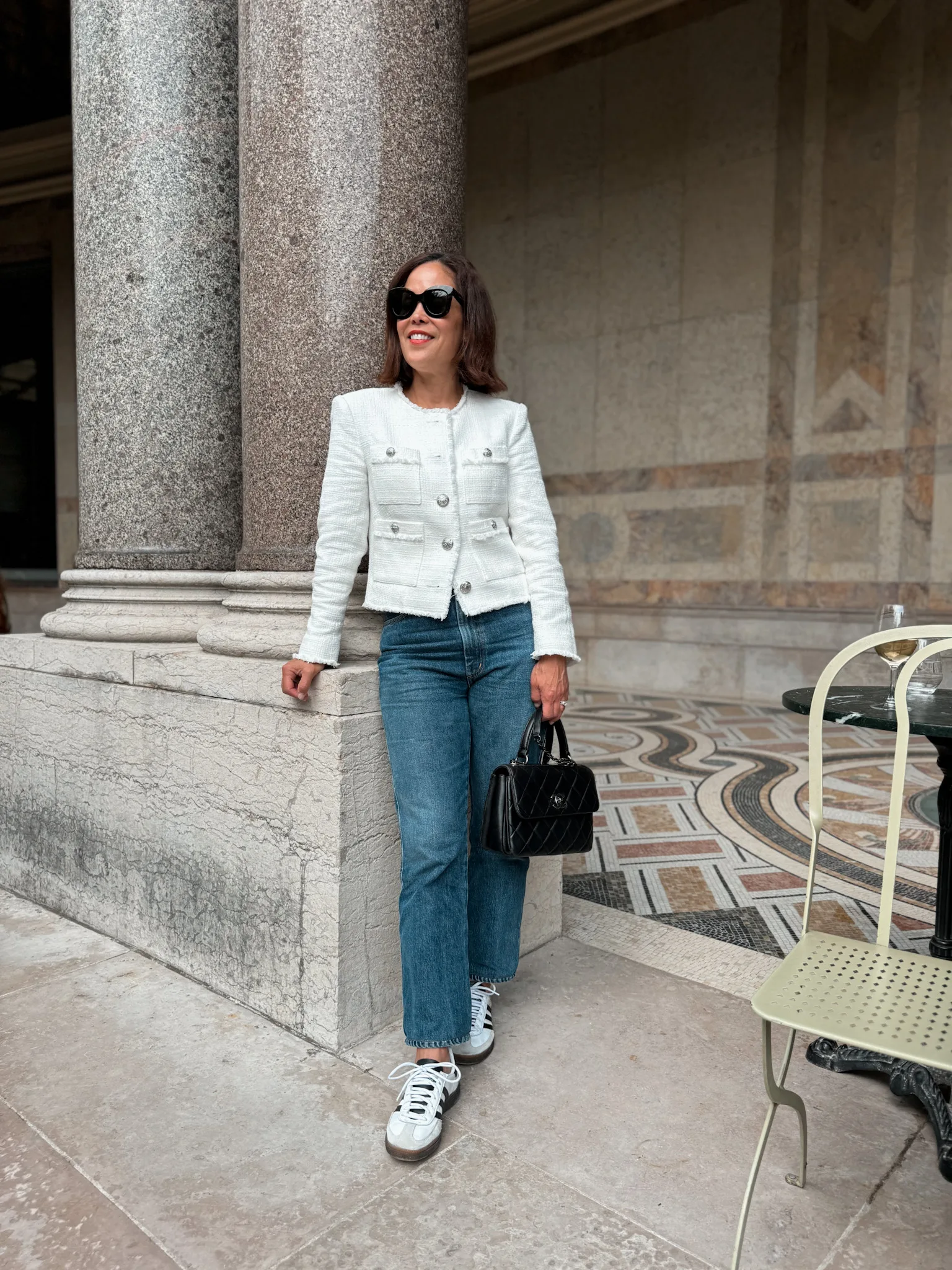 Lady standing wearing tweed jacket and denim with sneakers.
