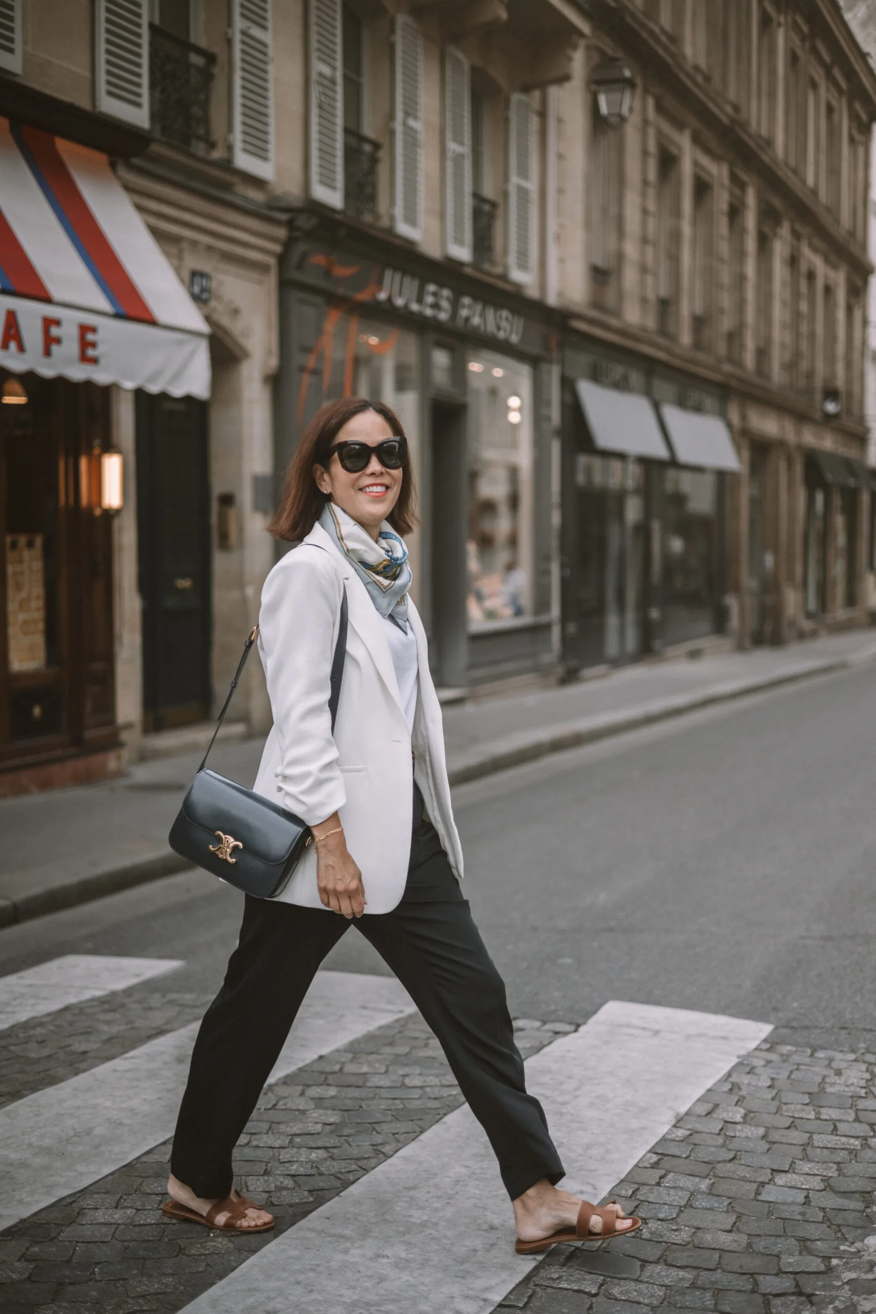 Woman walking across the street wearing navy pants in Paris.