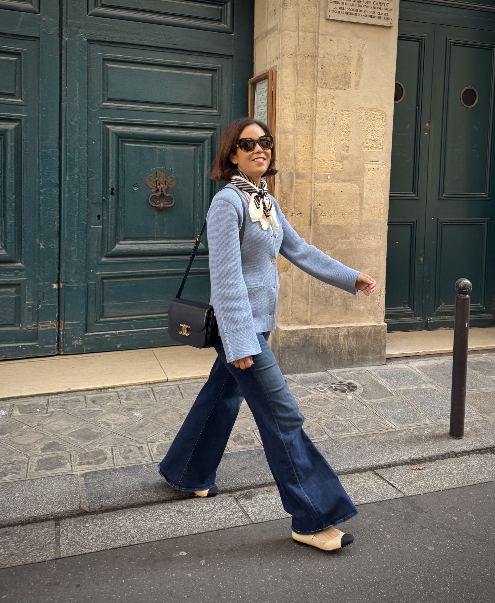 Woman wearing wide leg denim with ballet flats and cardigan in front of green door.