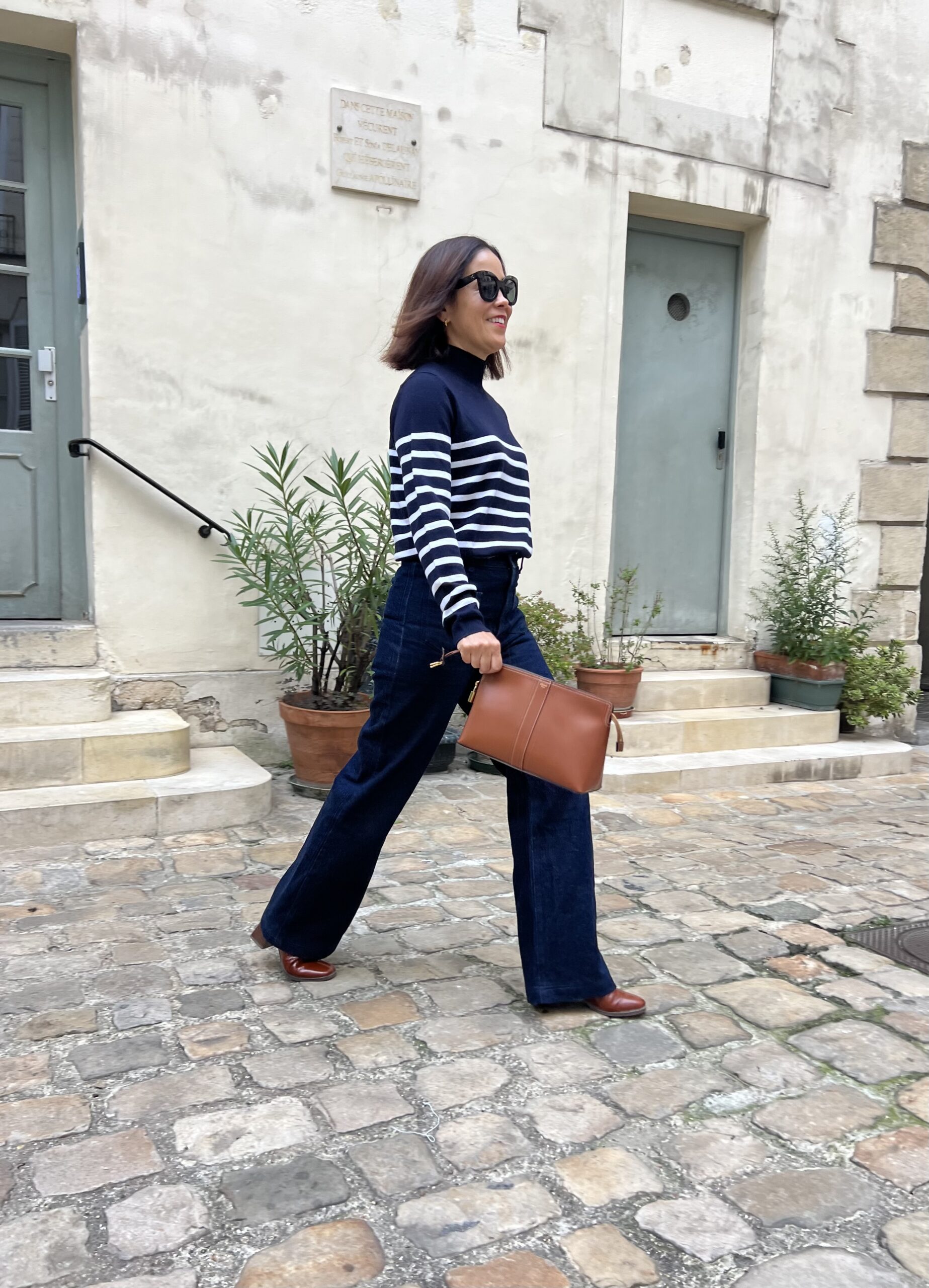 Woman wearing stripe turtleneck with brown clutch walking around.