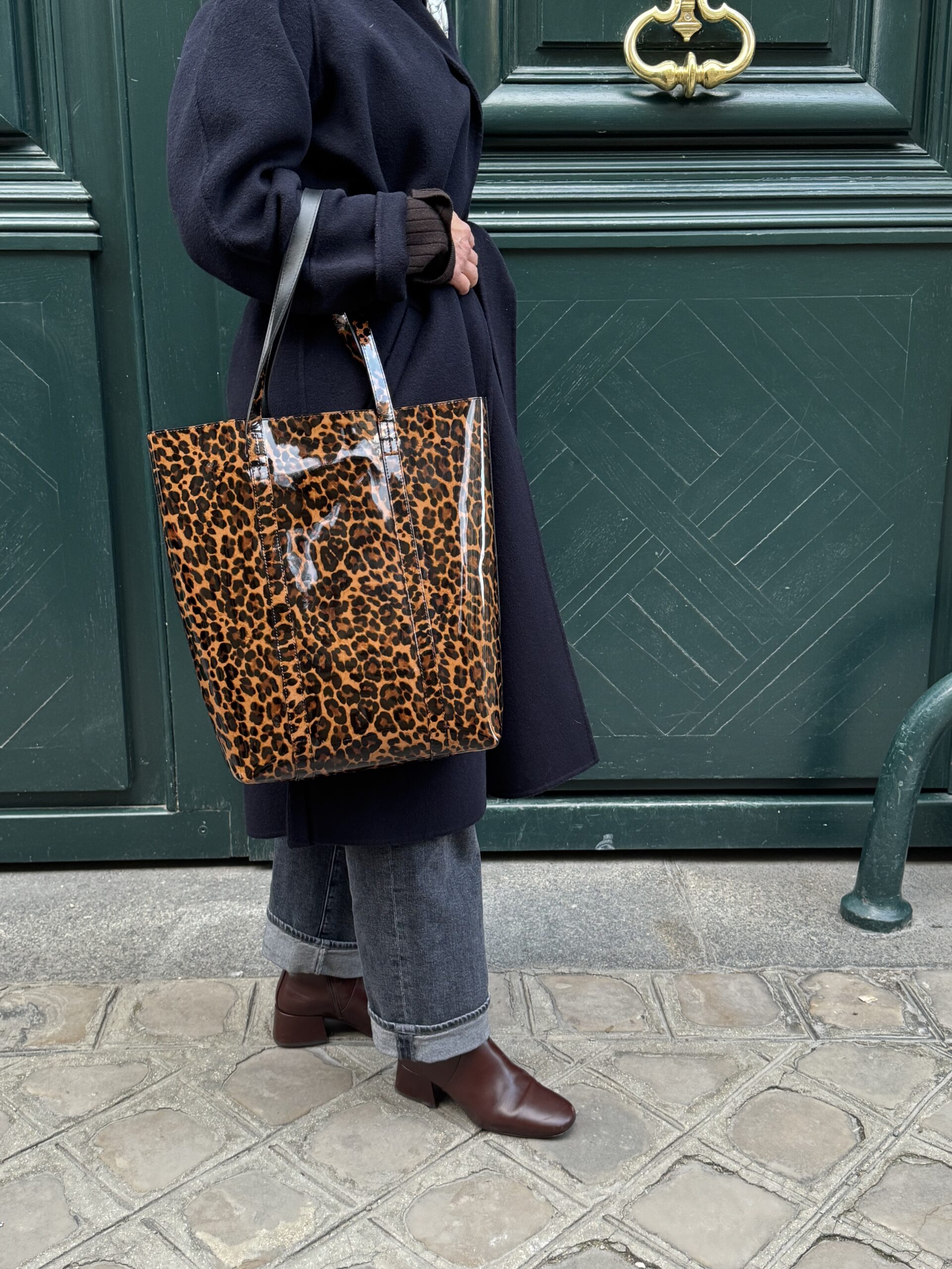 Woman holding animal print tote bag wearing black denim and brown boots.