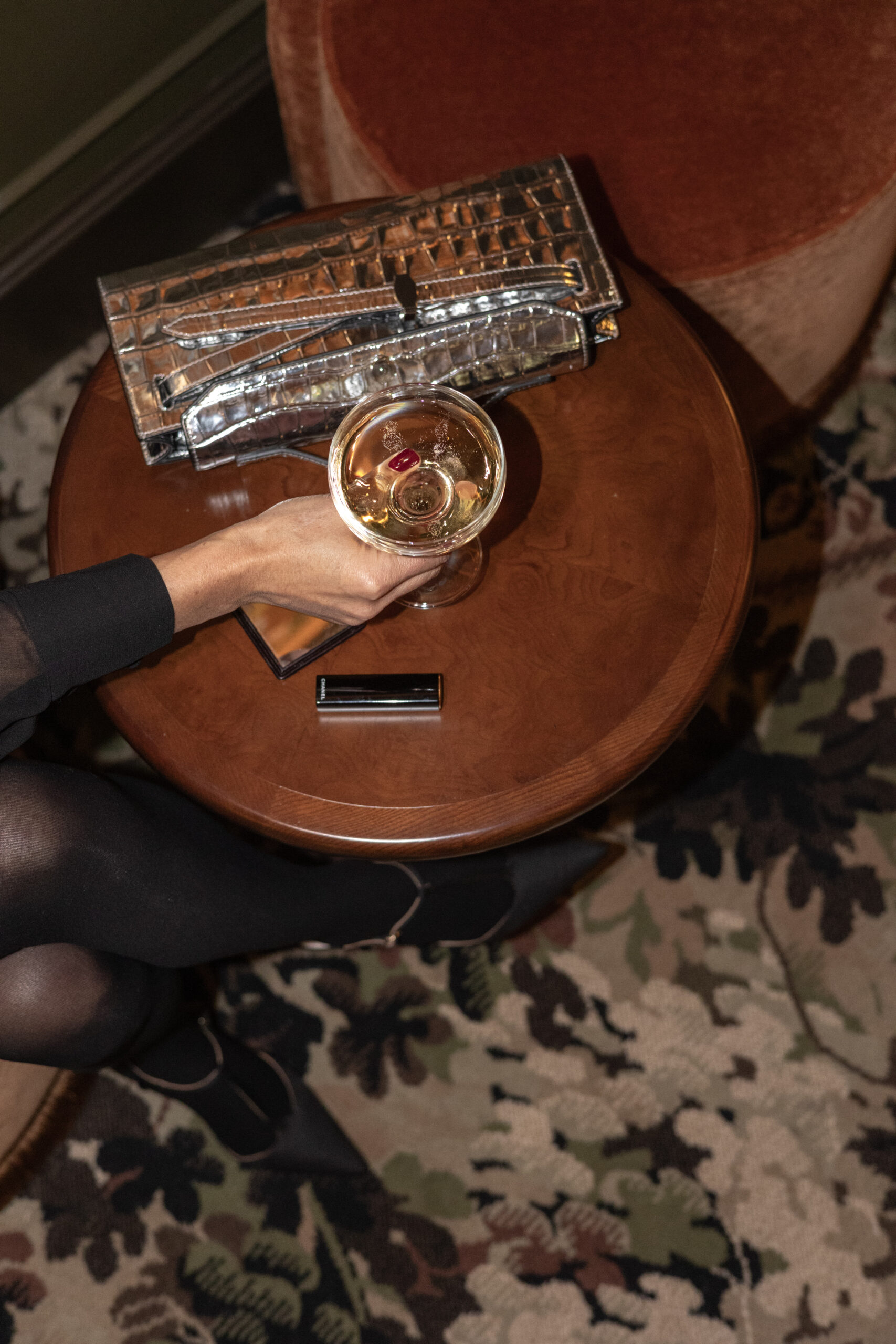Woman holding glass of champgane with a purse on the table.