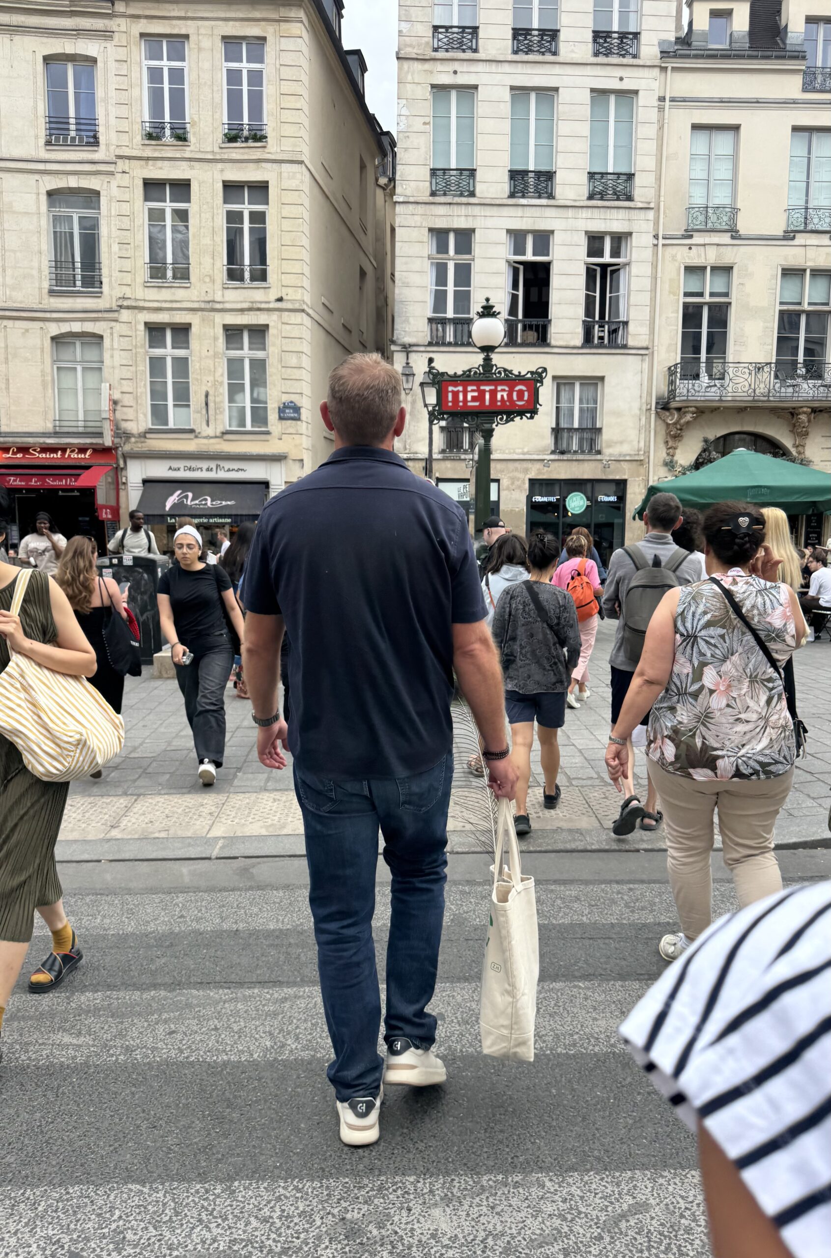 Man in navy shirt, denim, and sneakers walking in paris.