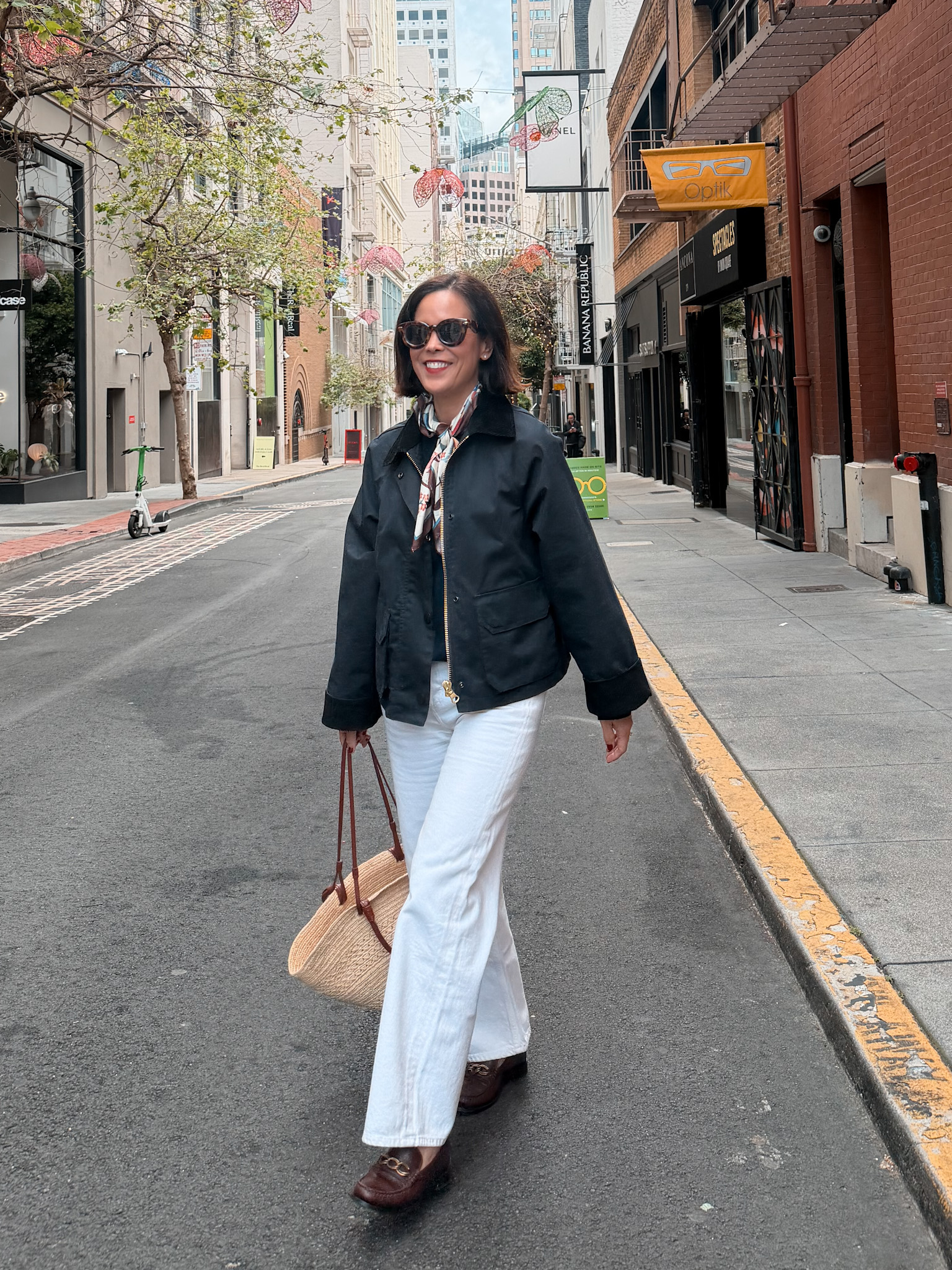 Chic spring outfit featuring a classic barn jacket styled with white denim, a silk scarf, and a straw tote for an effortless Parisian-inspired look
