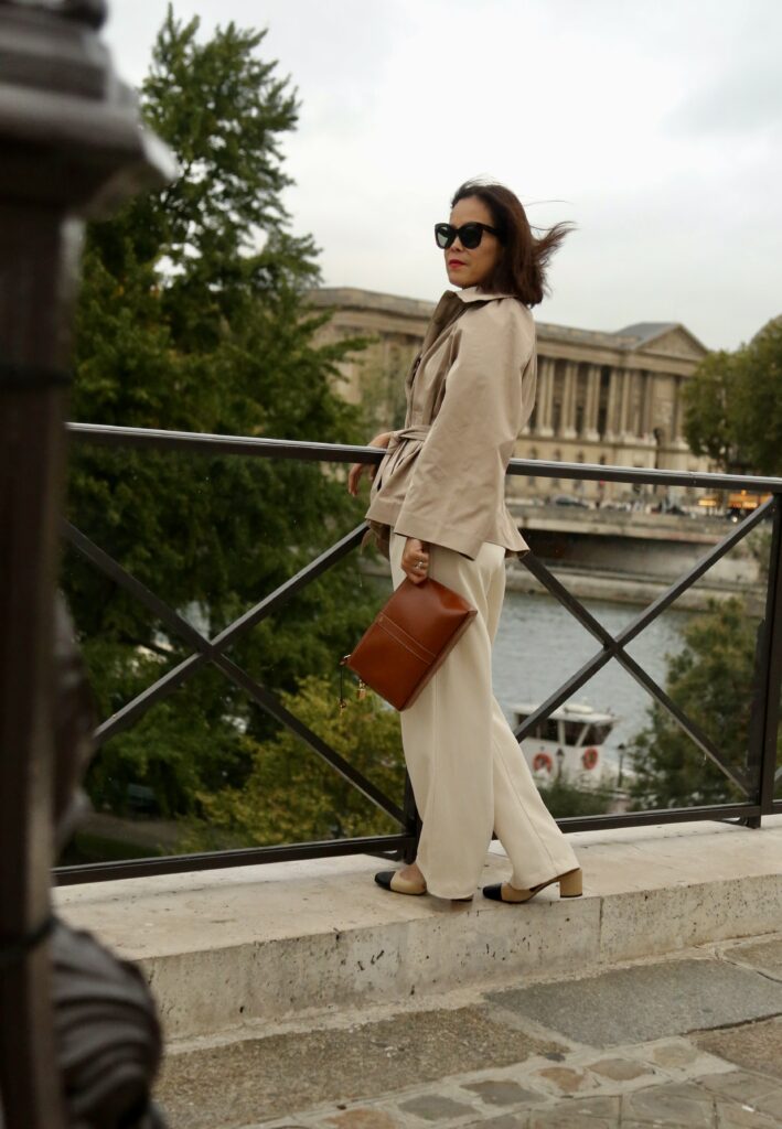 Noelani wearing slingback heels with cream wide-leg trousers and beige trench coat overlooking the Seine River Paris, French girl spring shoes.