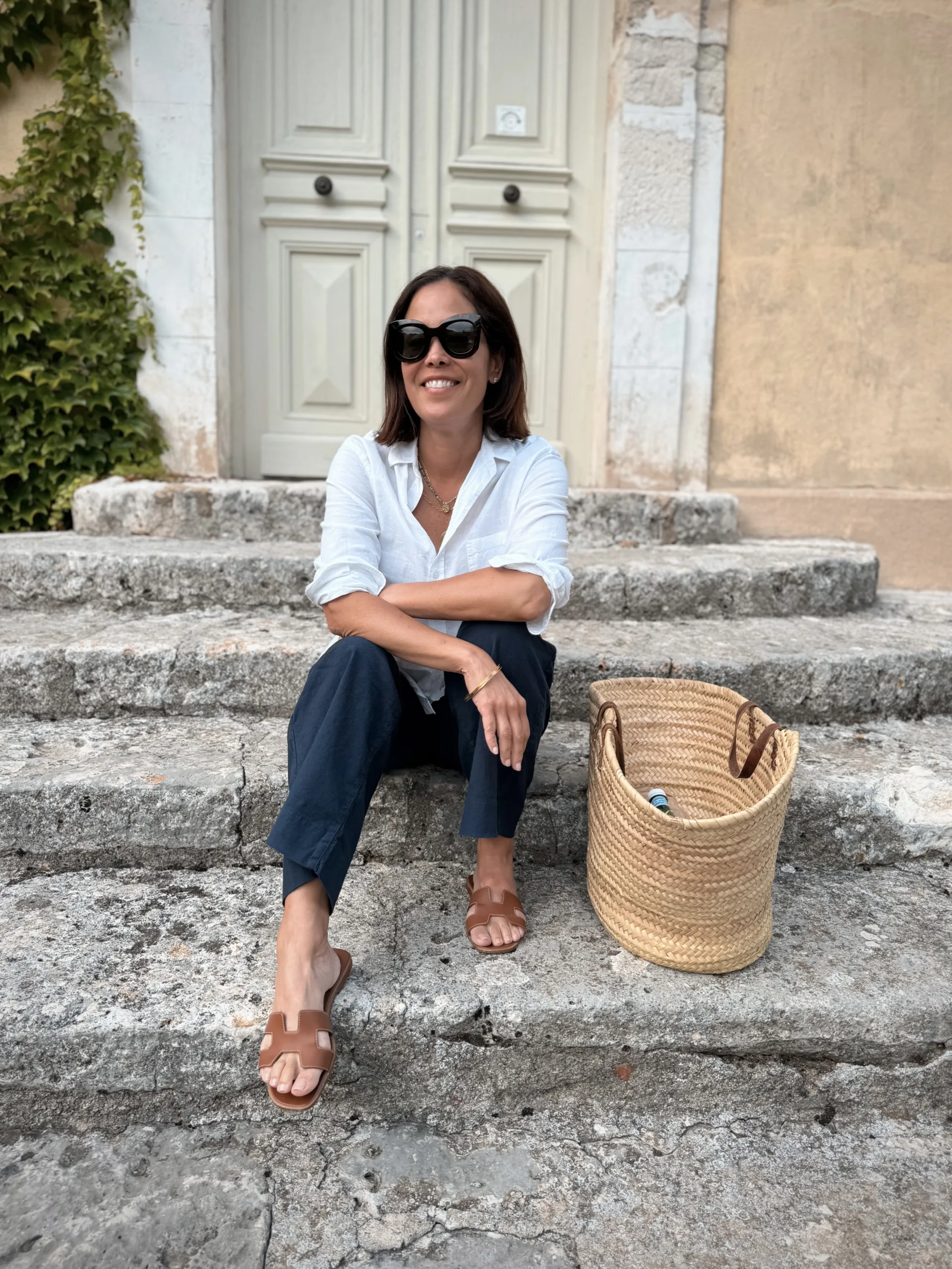 Woman sitting on steps with raffia tote bag for french summer essentials.