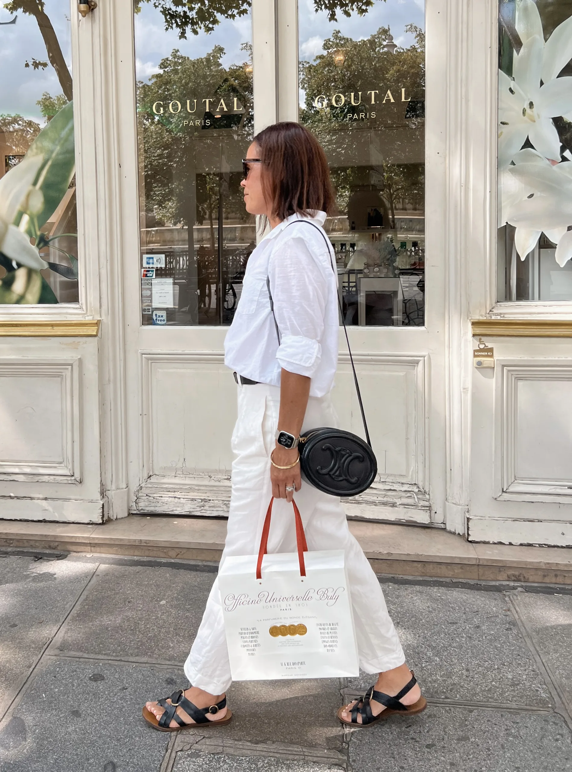 Woman in white top with cream pants and black sandals. 