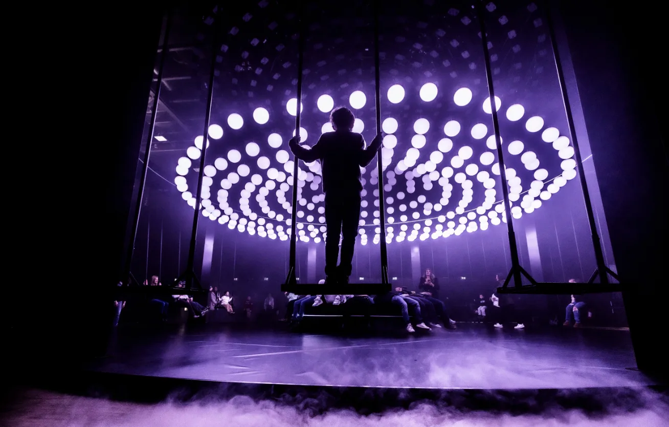 Person standing on a swing with a bunch of lights in Paris.