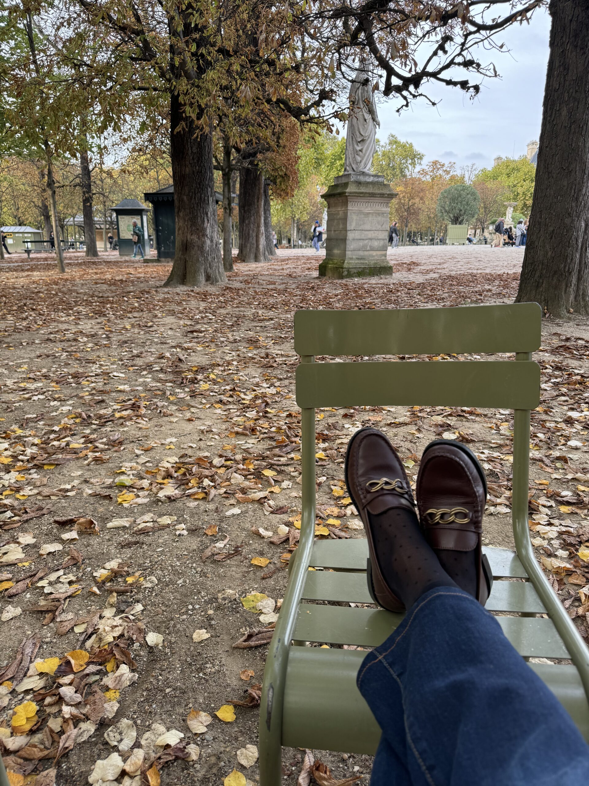 WOMAN WEARING LOAFERS SITTING IN LUXEMBOURG IN GREEN CHAIRS.
