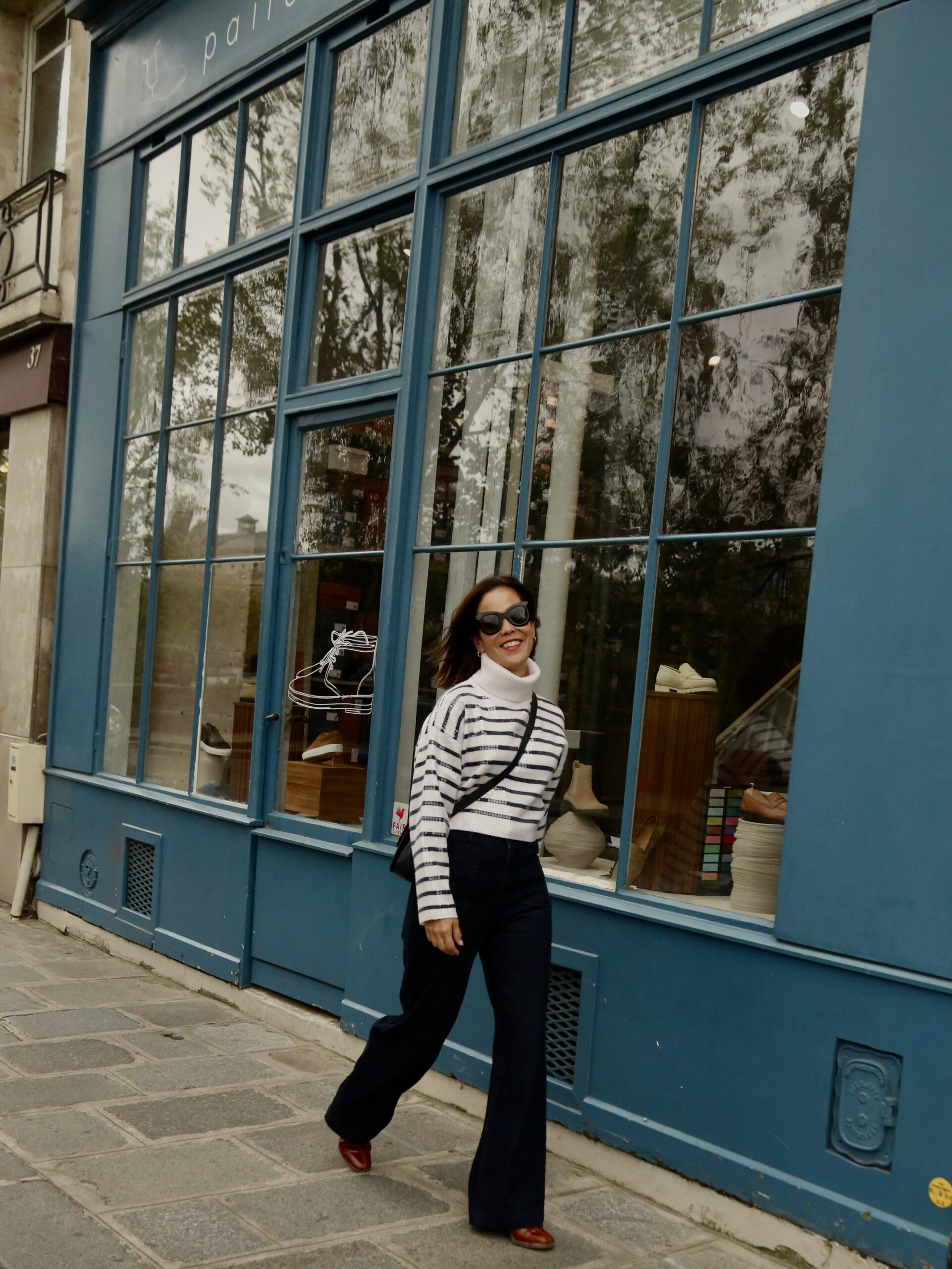 Woman wearing stripe sweater with crossbody bag, denim, and shoes walking in Paris during winter.