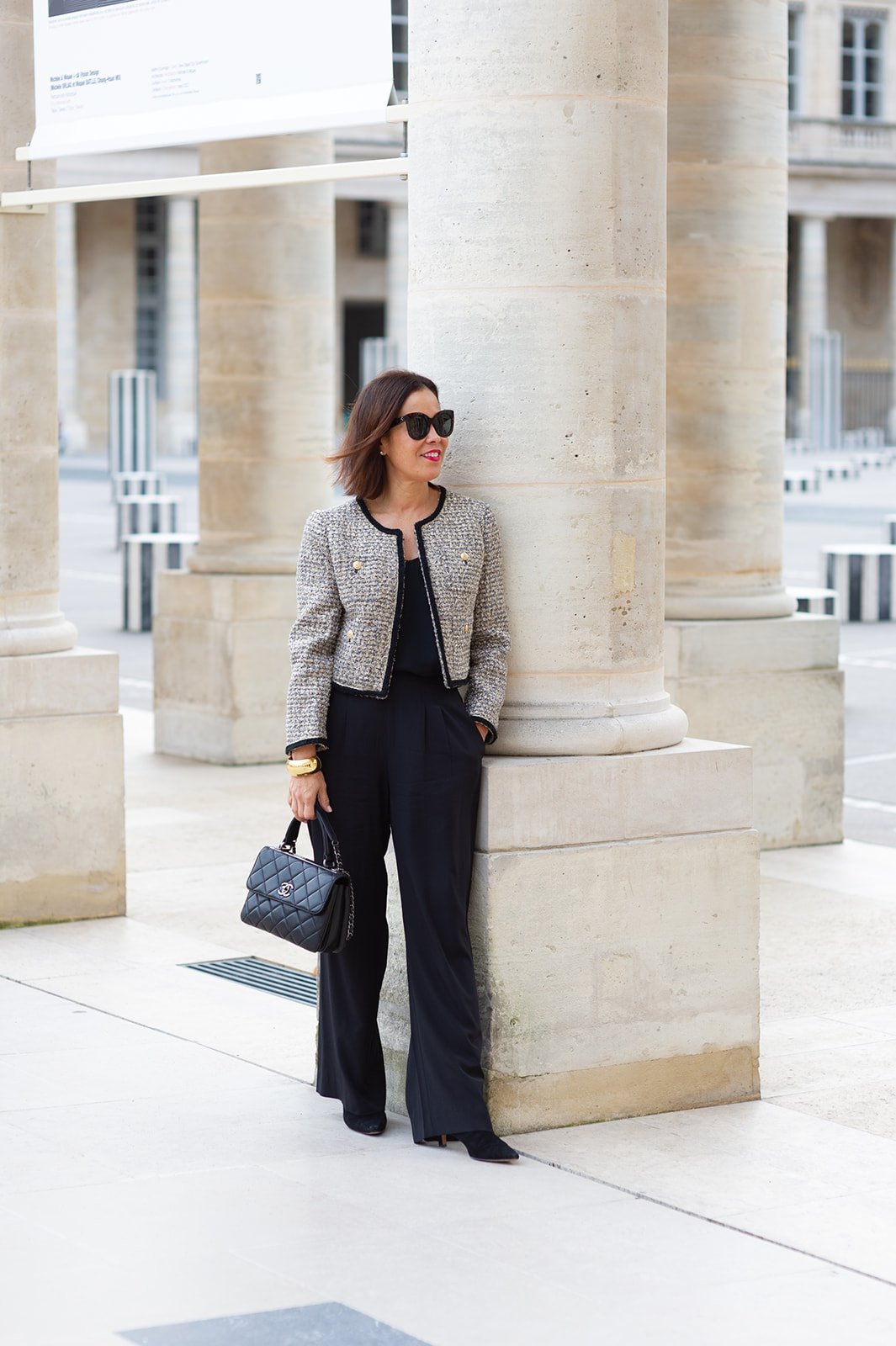 Woman wearing tweed jacket with black boots standing in palais royal garden.