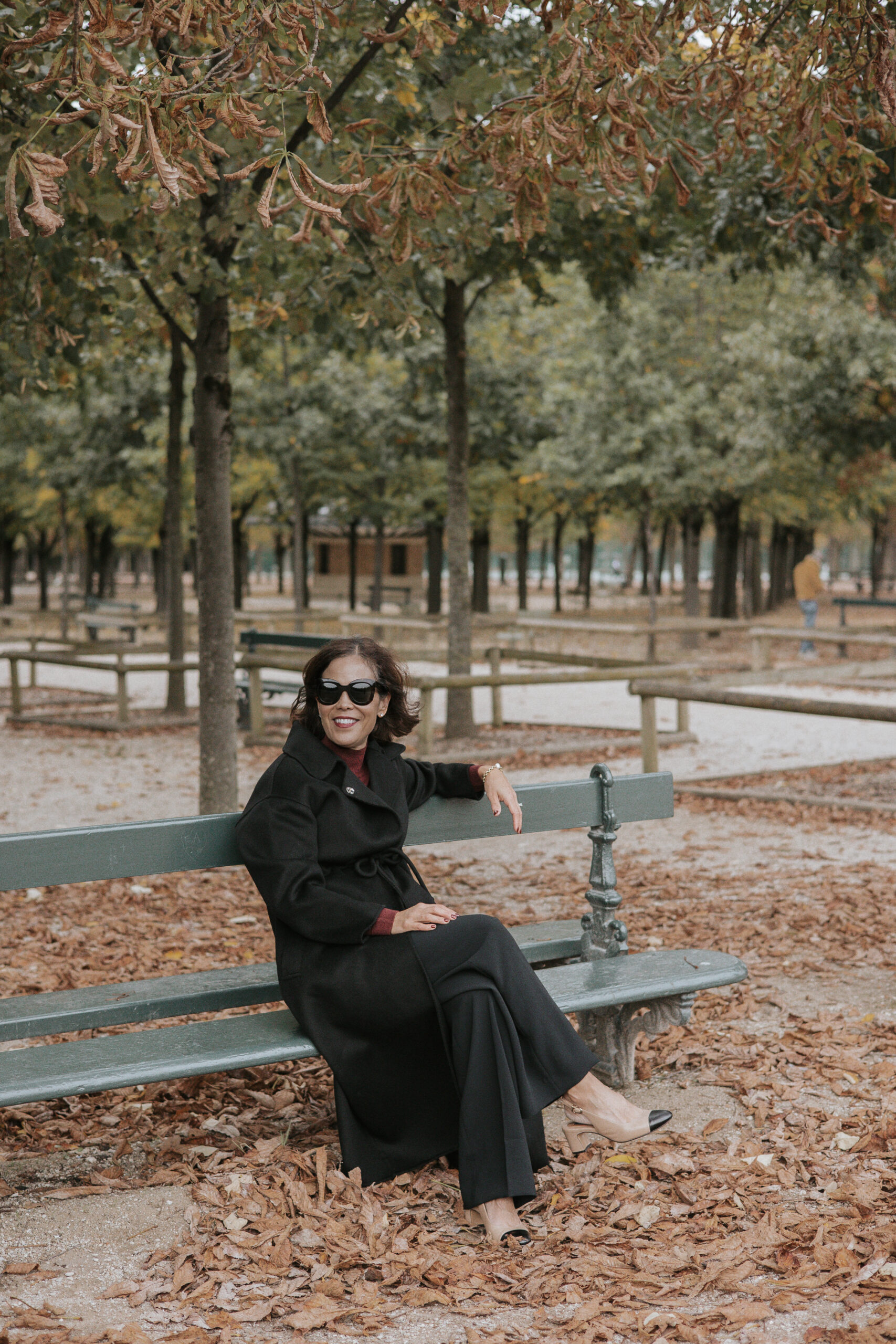 Woman sitting on a bench in the luxembourg gardens with a black wool coat.
