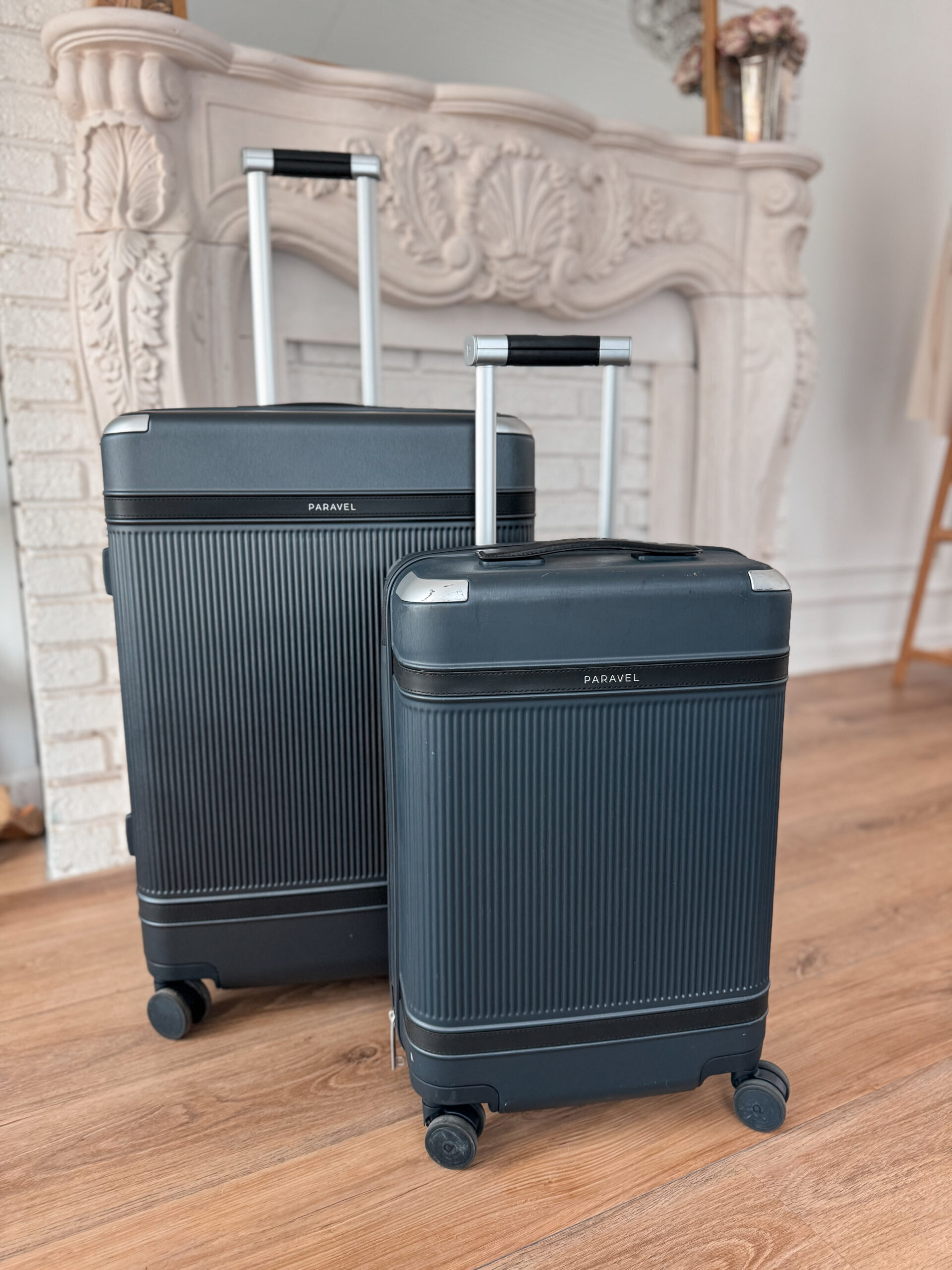 Two navy suitcases sitting in front of a fireplace.