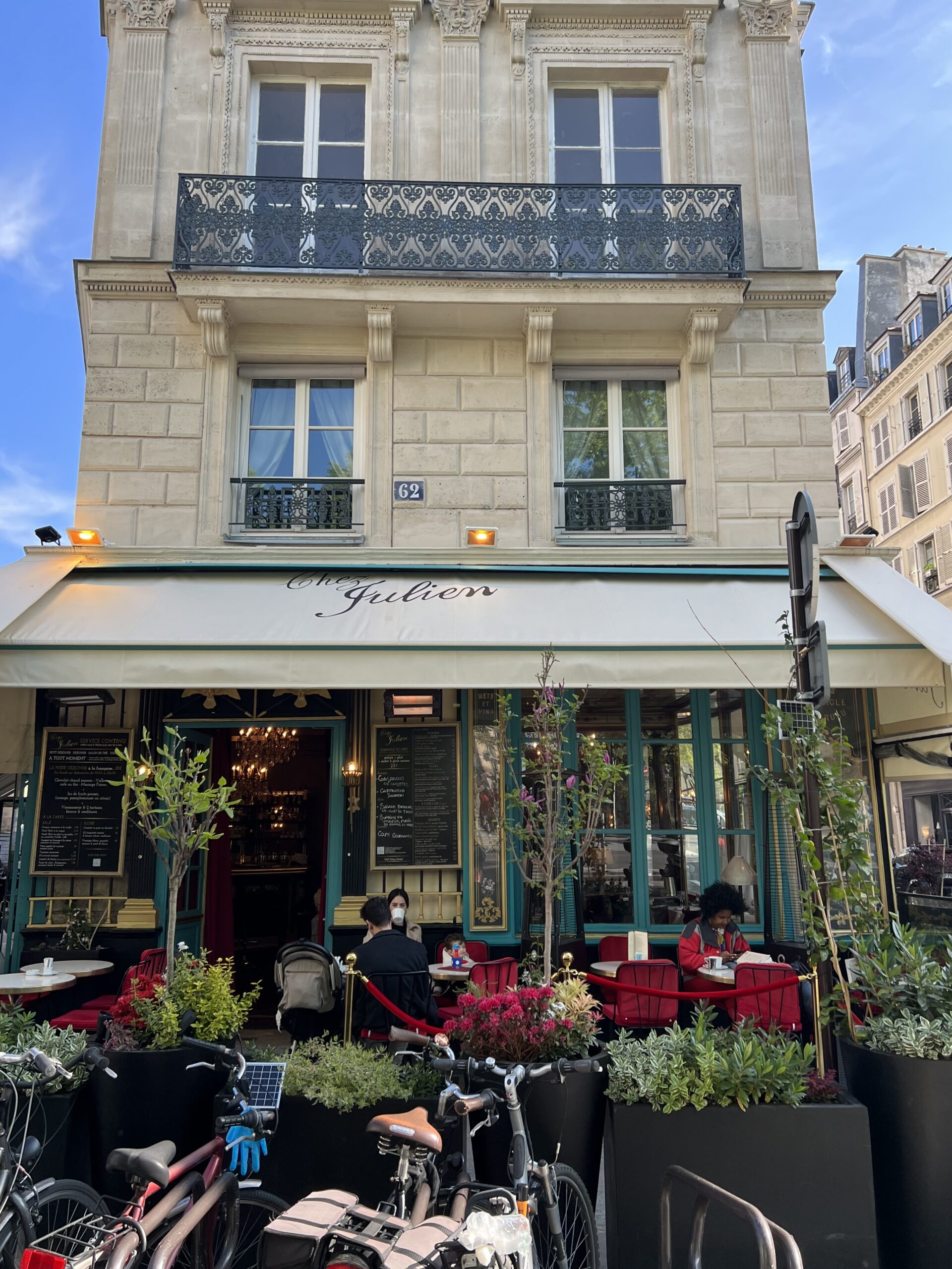Café Julien with cream awning, blue trim around windowns, red tablecovers and plants on terrace in paris.