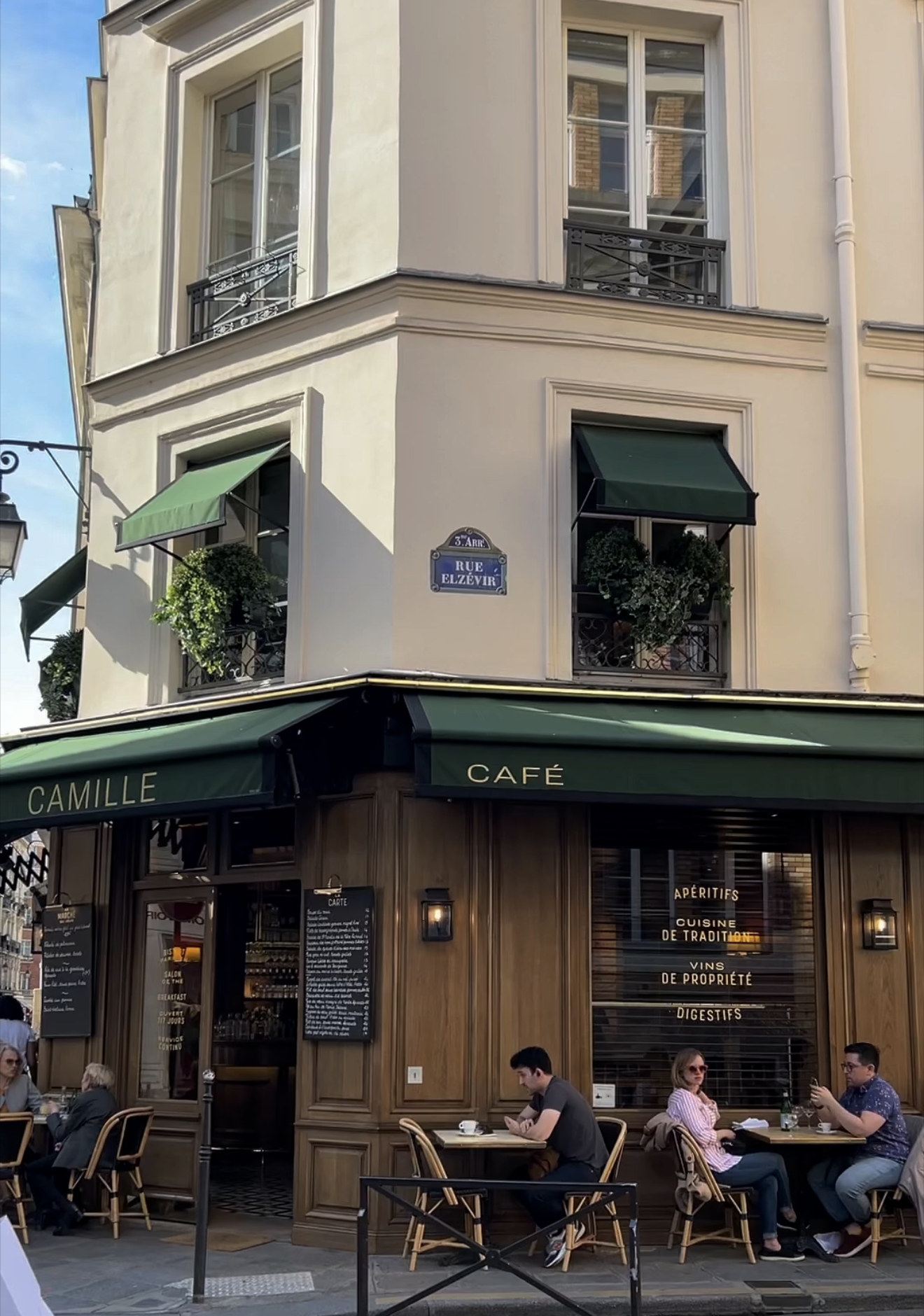 Exterior shot of Camille cafe in Paris on street corner with green awning.