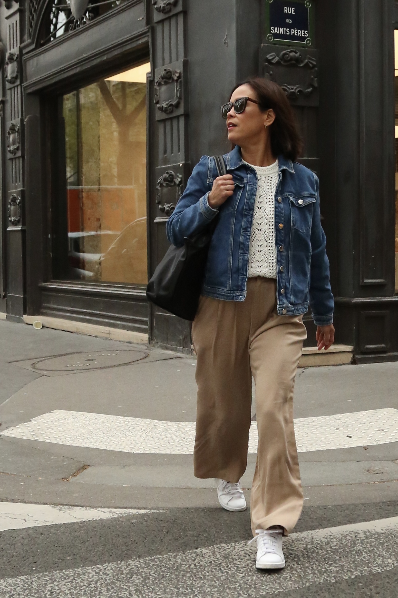 Parisian woman wearing a denim jacket, neutral trousers, and white sneakers while walking in Paris