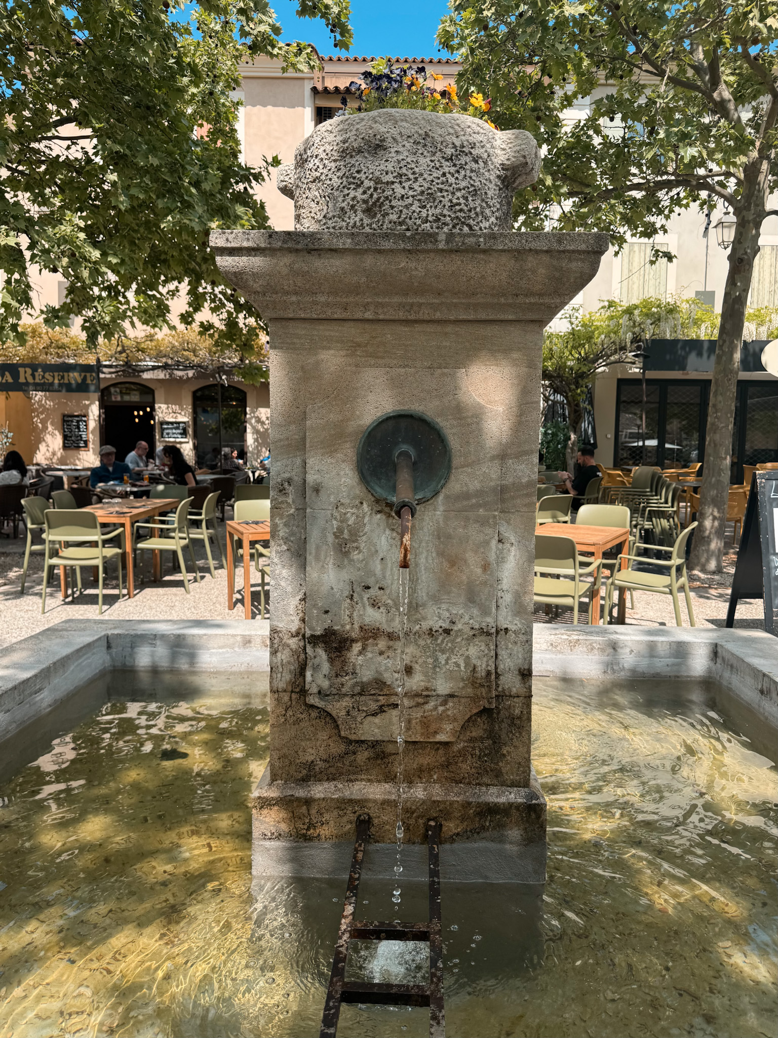 Stone fountain in the main square of Lourmarin surrounded by cafés and plane trees