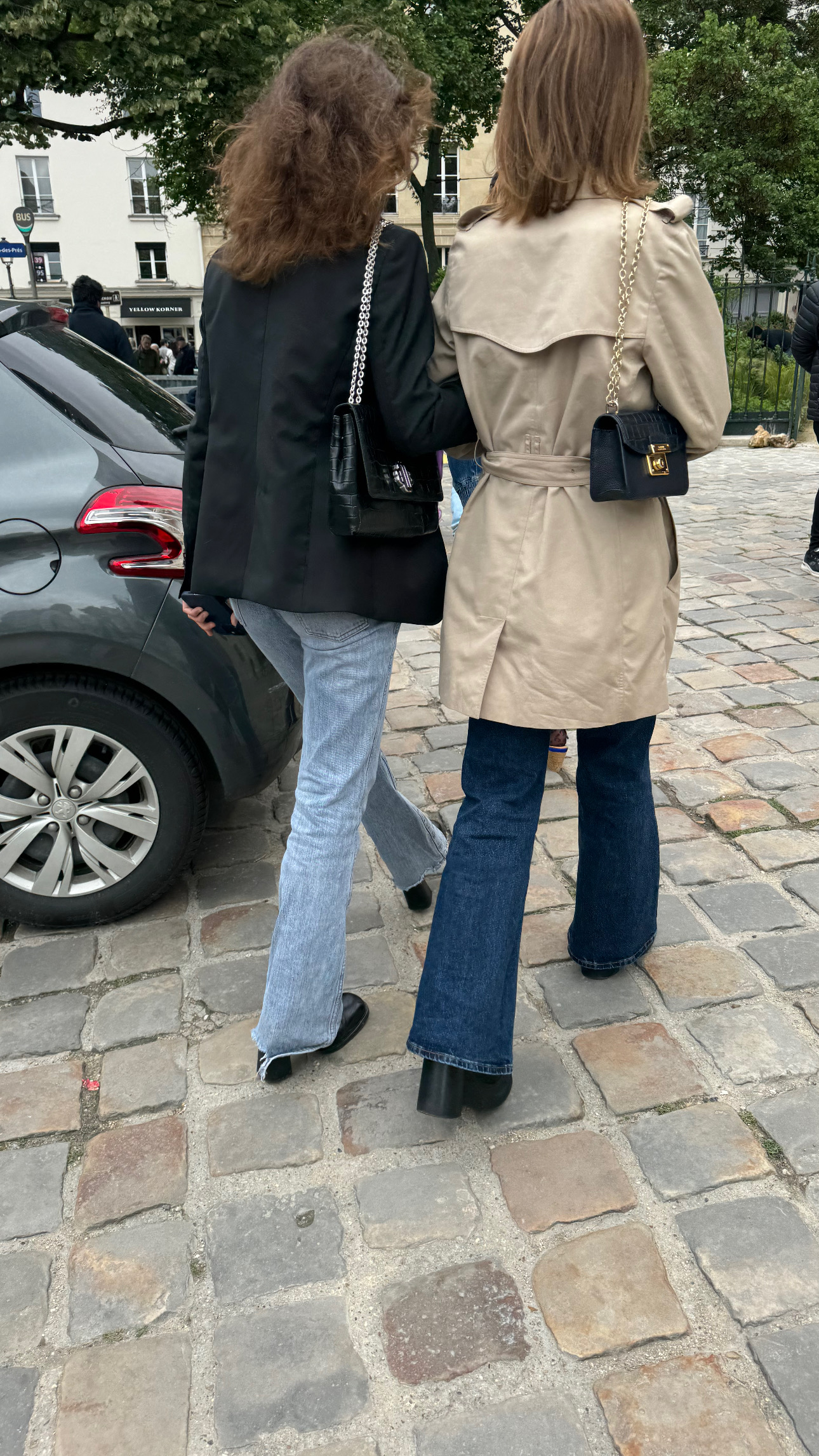French women style in Paris in March wearing a trench coat and blazer with denim and classic crossbody bags on cobblestone streets