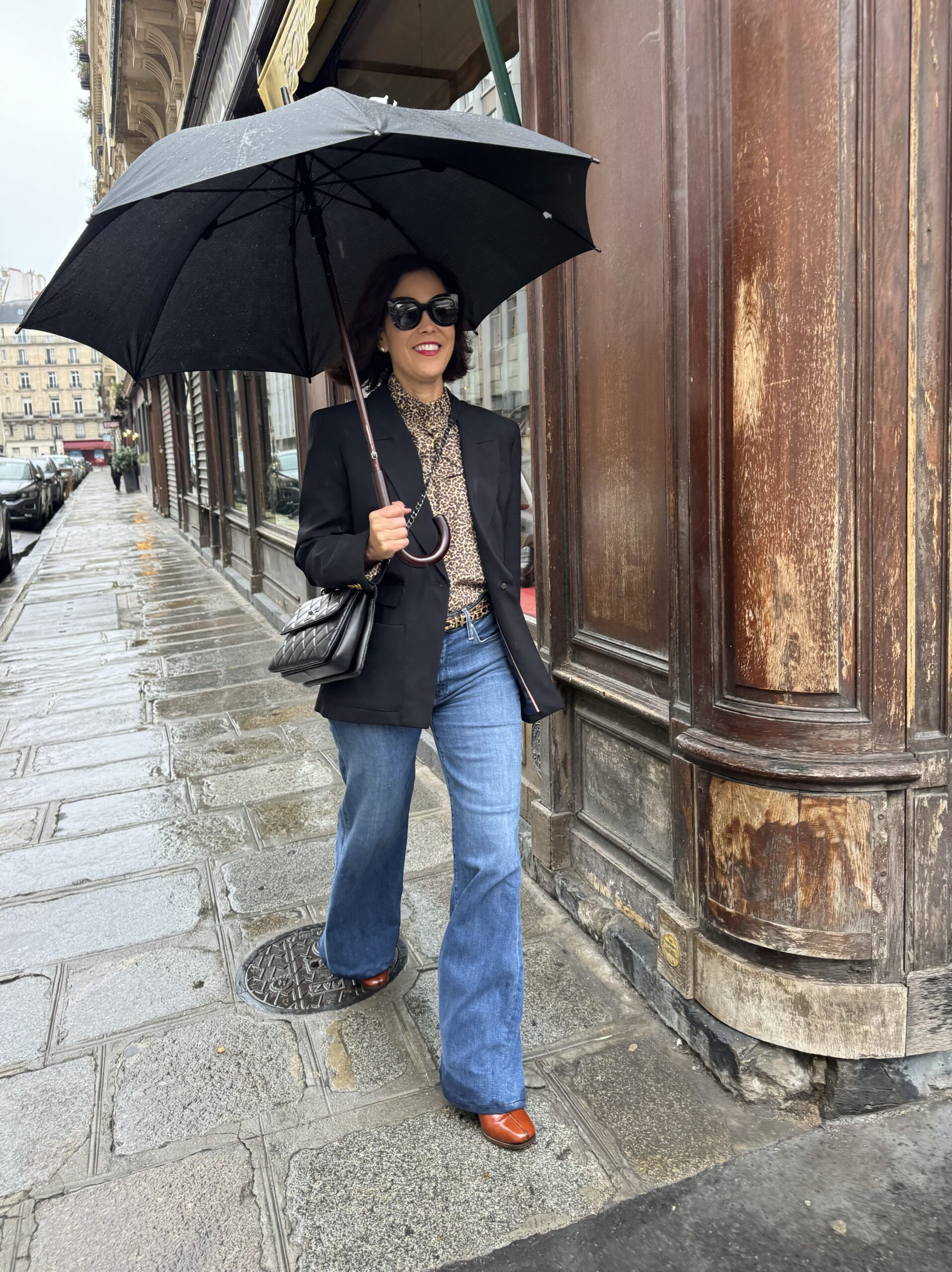 Woman walking with umbrella wearing boots and blazer in Paris during rain.