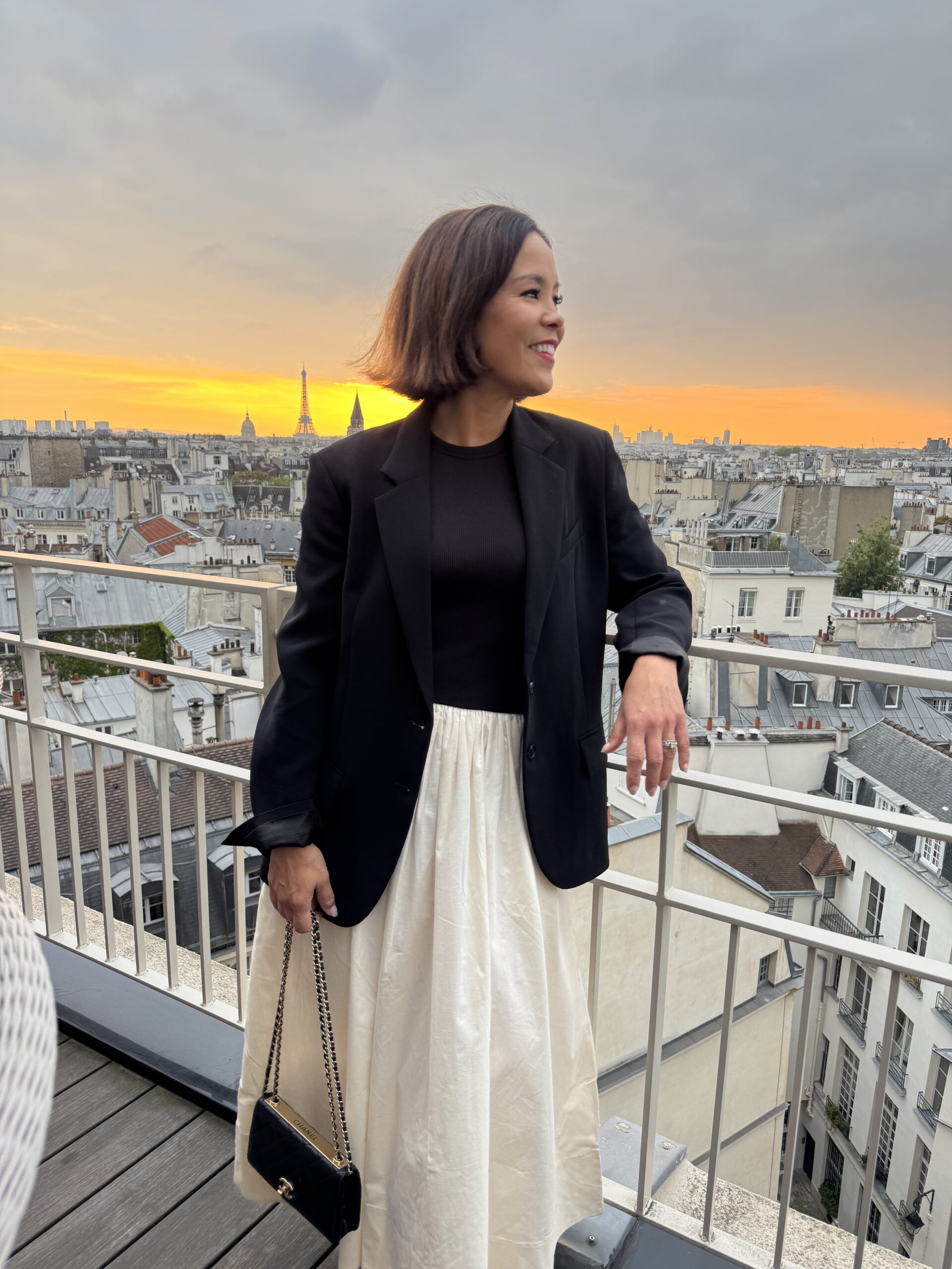 Woman standing on Paris rooftop with eiffel tower in the background during the evening in Paris.
