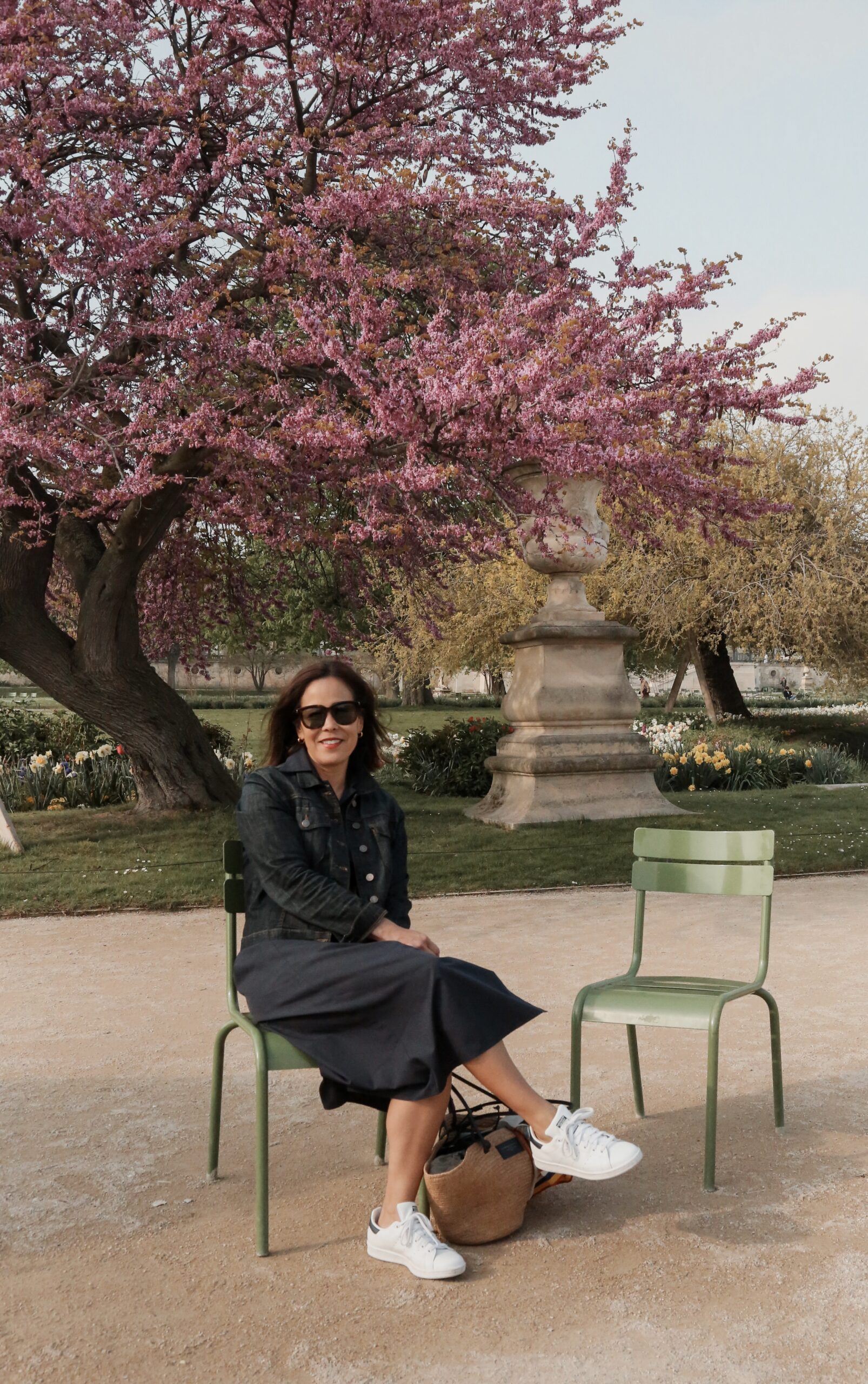Woman sitting in Tulieries garden in Paris in spring with cherry blossoms in background.