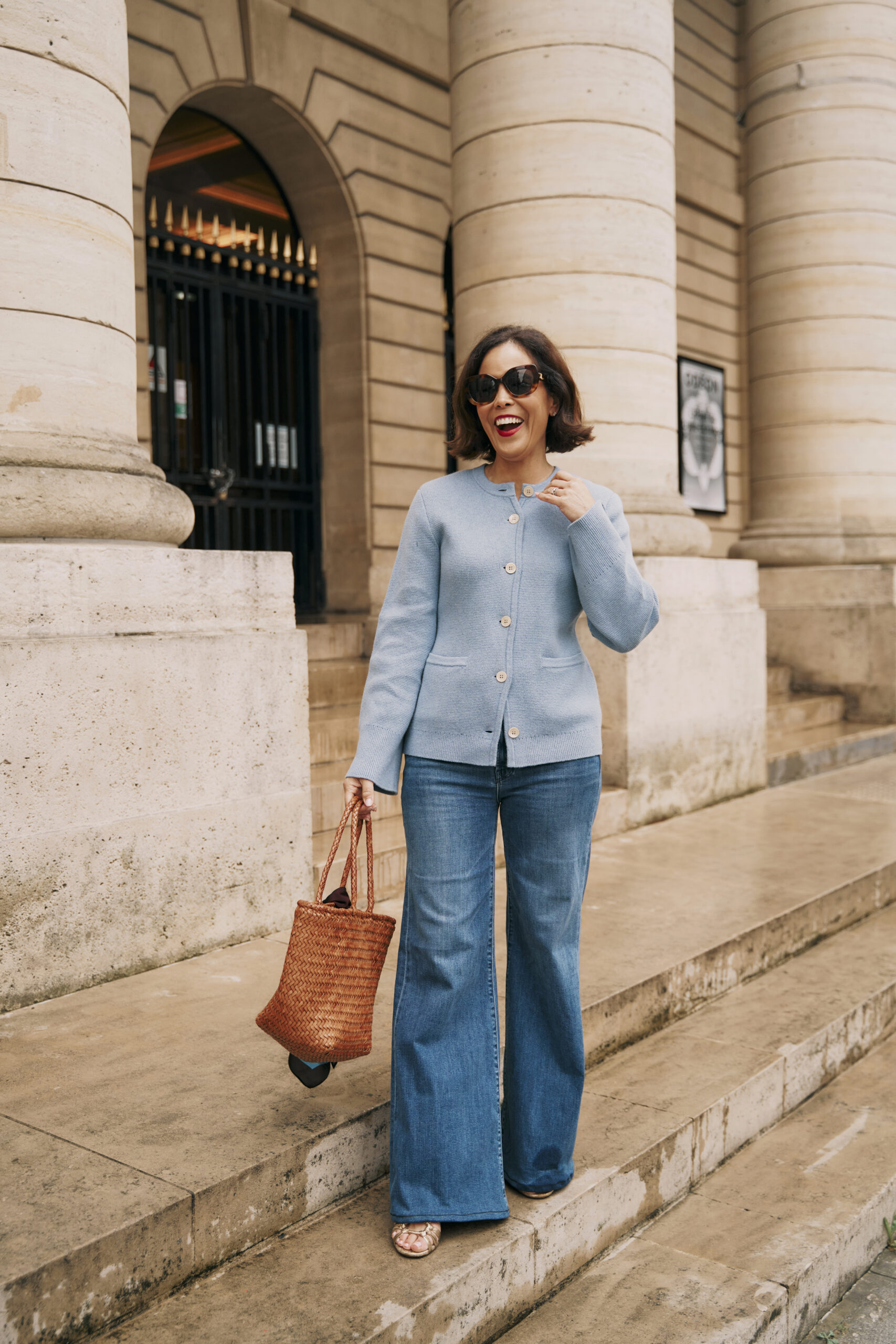 Woman wearing blue sweater with denim and brown bag with silk scarf in paris showing a spring french capsule wardrobe.