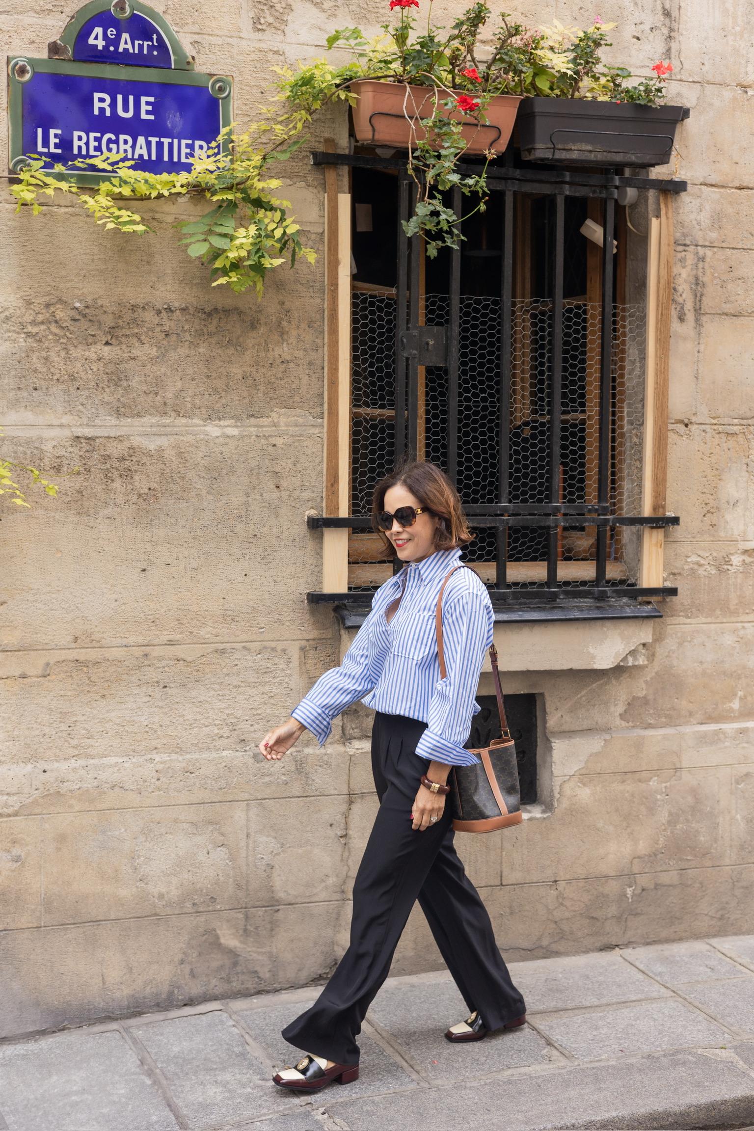 French spring wardrobe outfit with striped top, black trousers, and loafers walking in Paris