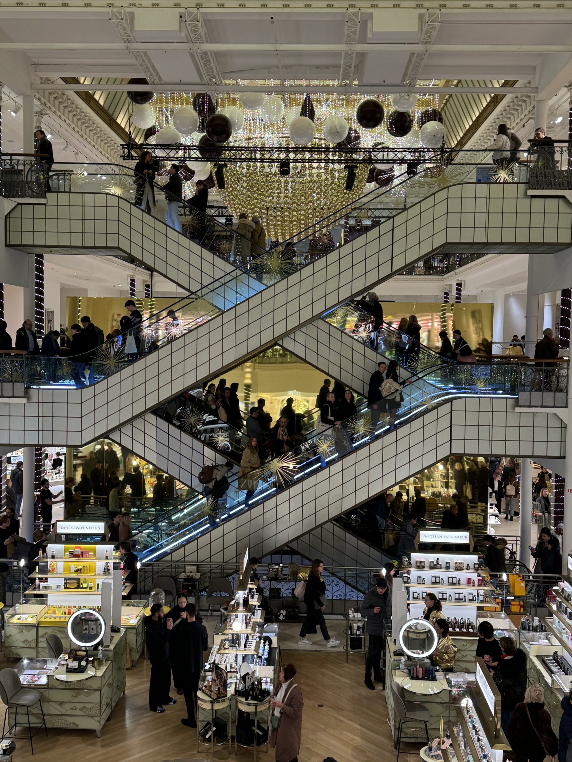 Interior of Le Bon Marché department store in Paris with escalators and holiday decor.