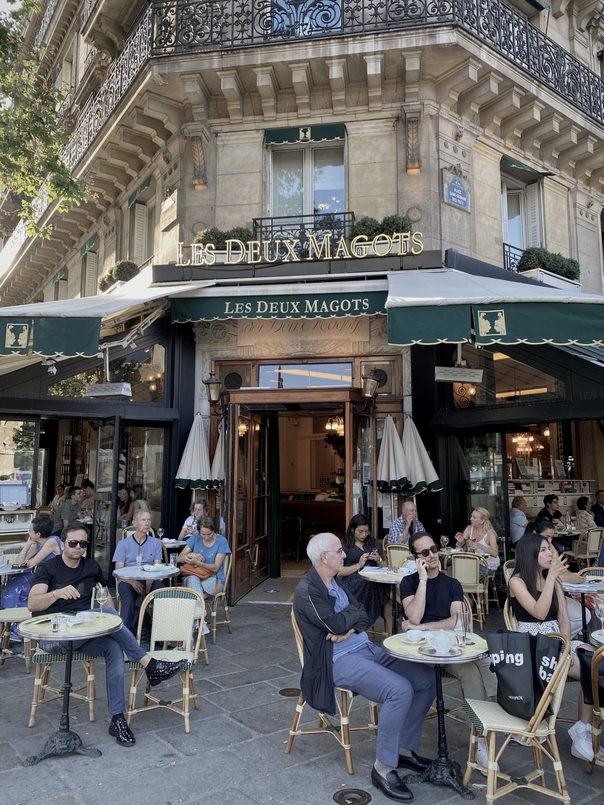 Les Deux Magots café in Saint-Germain-des-Prés with people seated on the terrace enjoying coffee and wine.