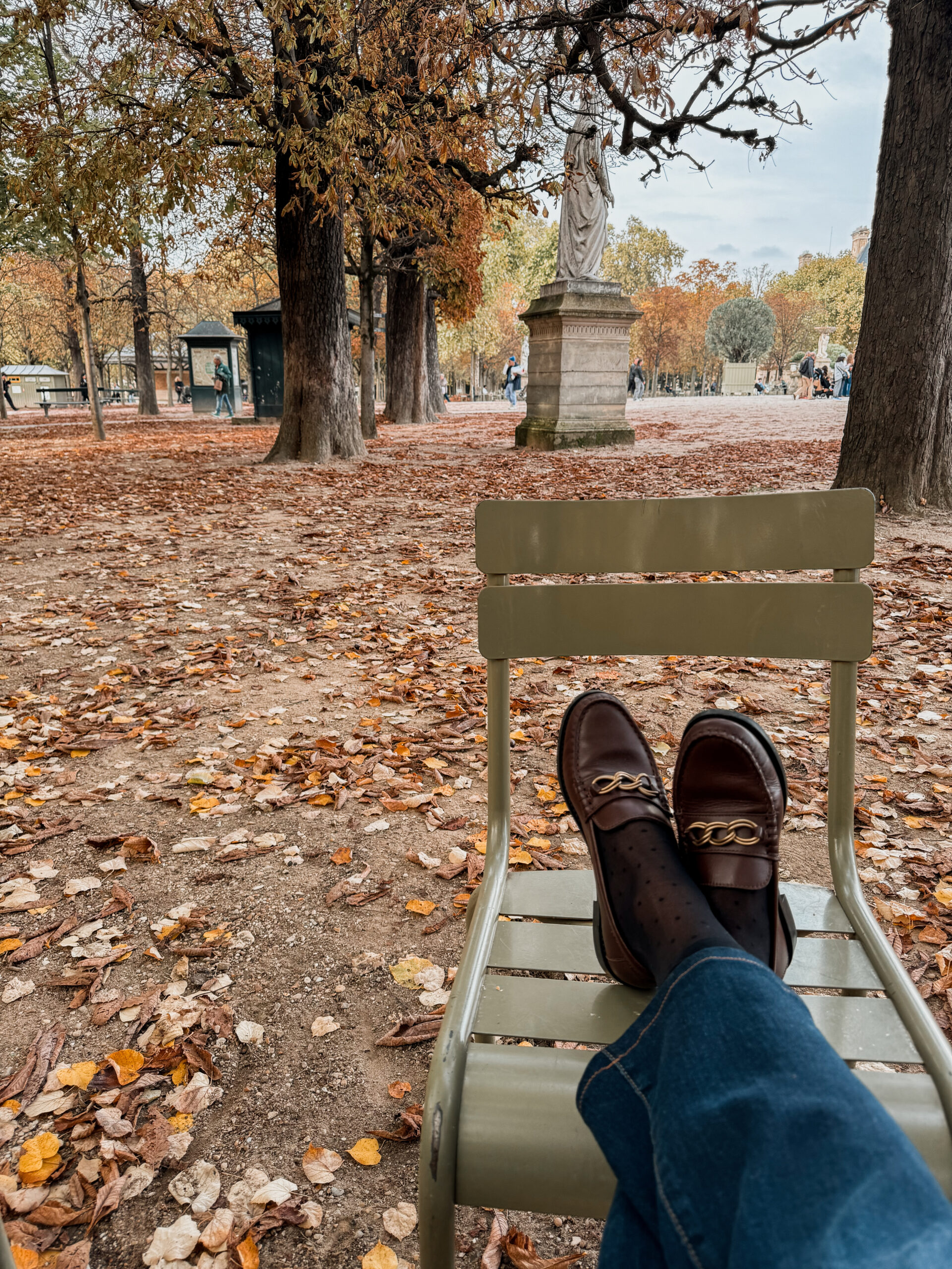 Relaxing on a green chair in the Luxembourg Gardens in Paris during autumn, a favorite spot for people watching in Saint-Germain-des-Prés