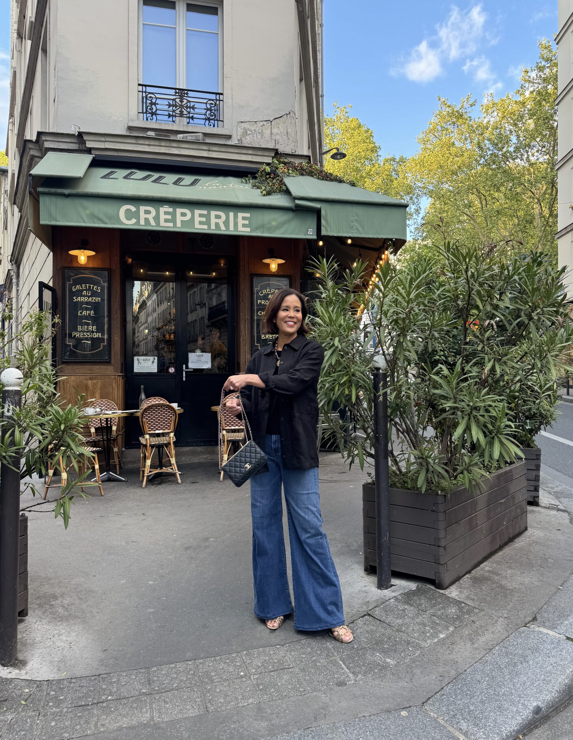 Paris spring outfit in April with black light jacket, dark jeans, and crossbody bag outside a café