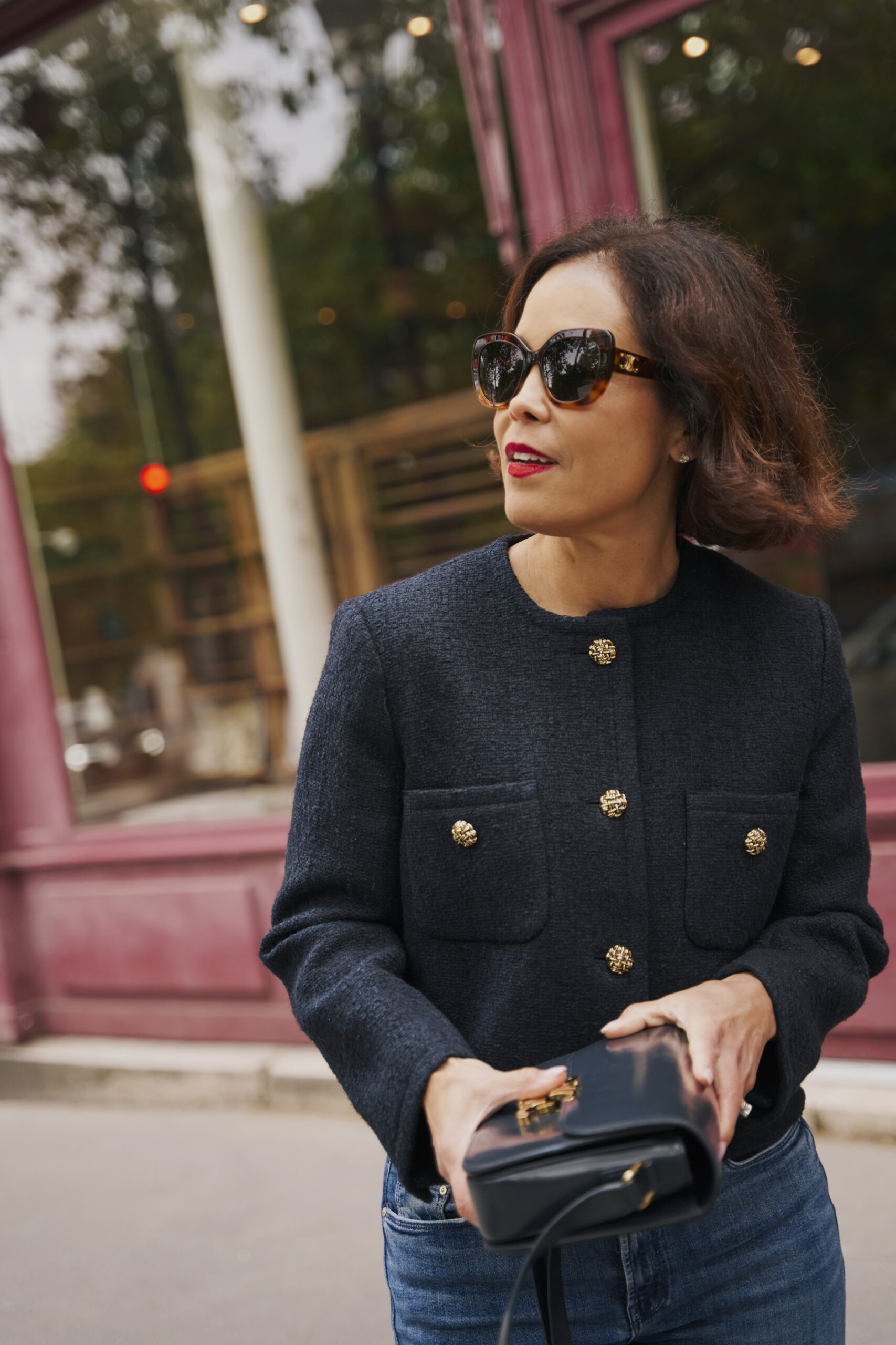 Parisian fashion outfit in April featuring black jacket with gold buttons, jeans, sunglasses, and structured handbag