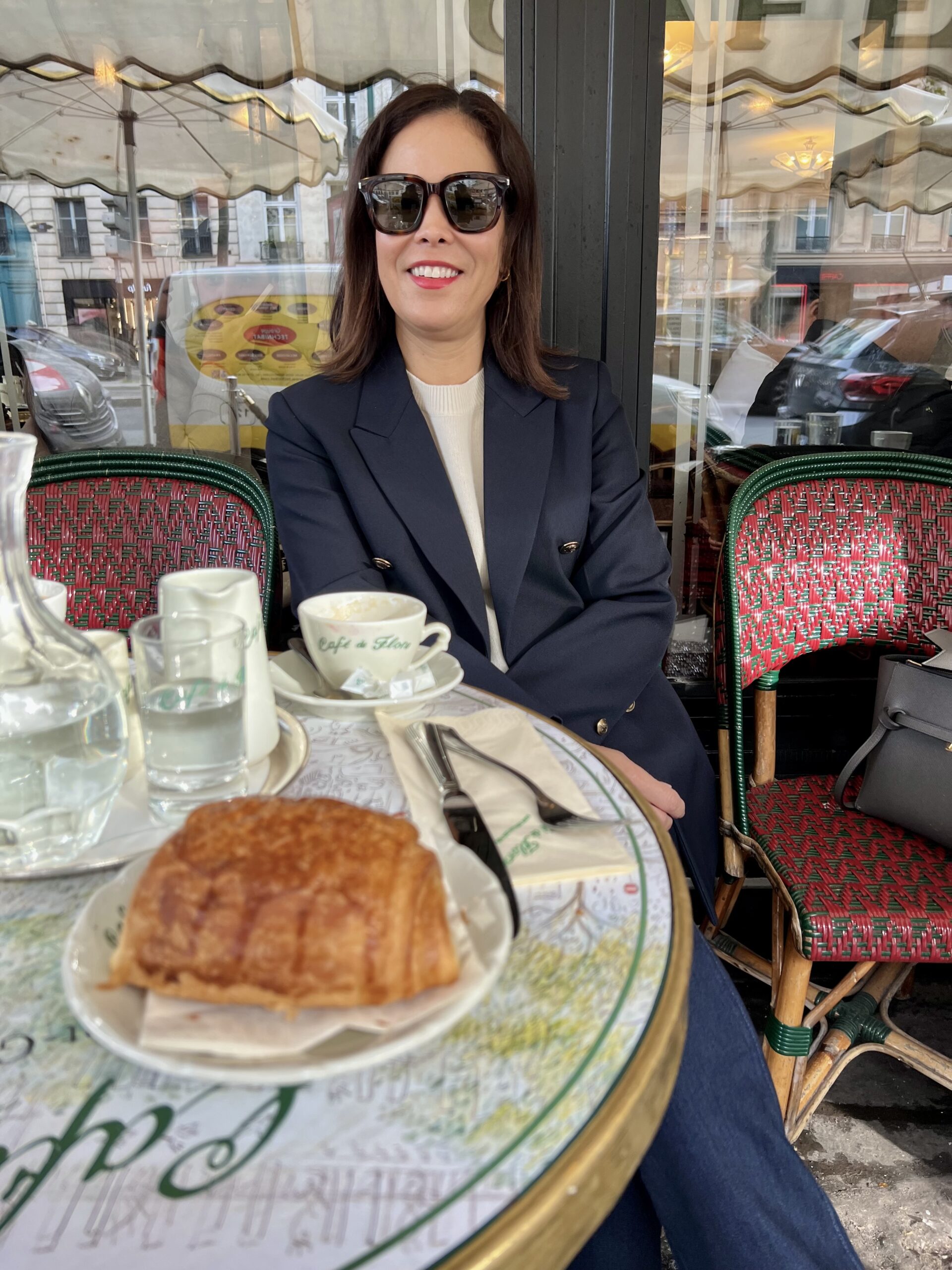 Woman sitting at cafe de flore with a croissant and cup of coffee on the table.