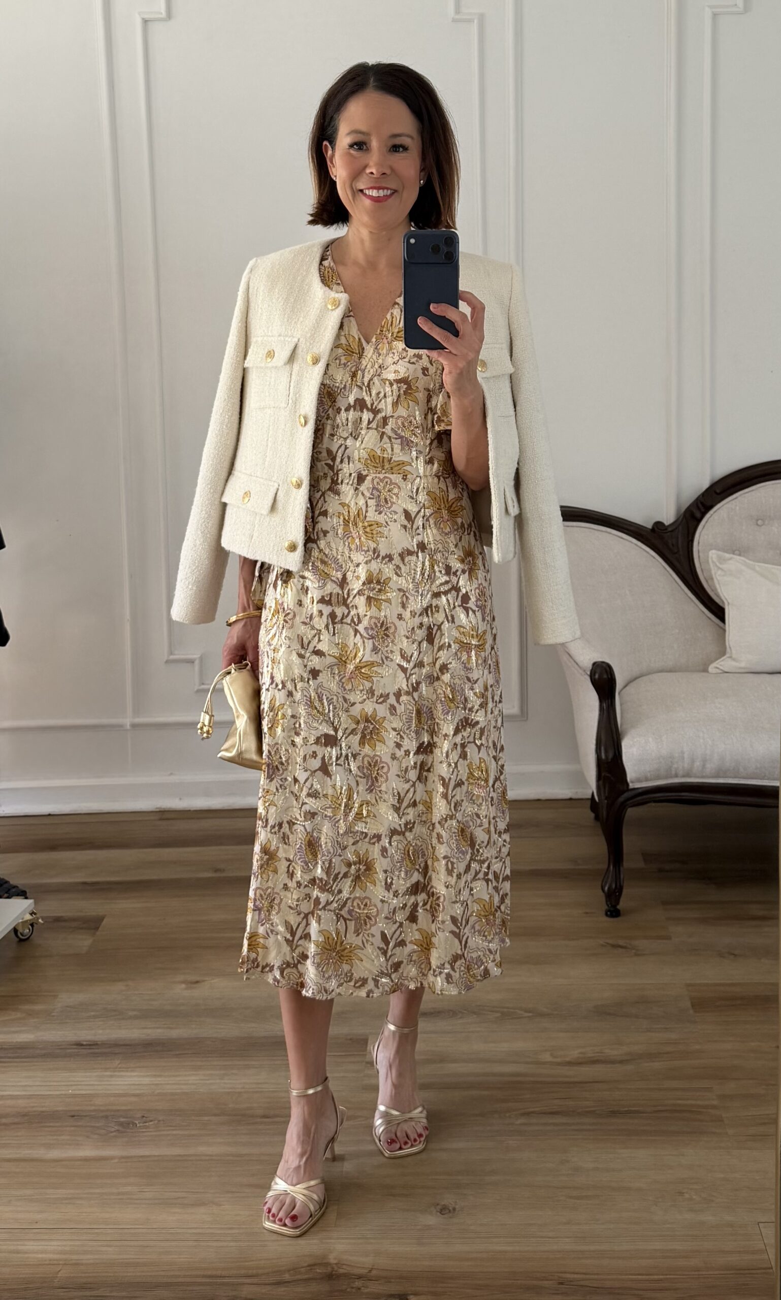 Cream tweed jacket layered over a gold and cream floral midi dress with gold strappy heels and a gold mini bag — an elegant spring occasion outfit

