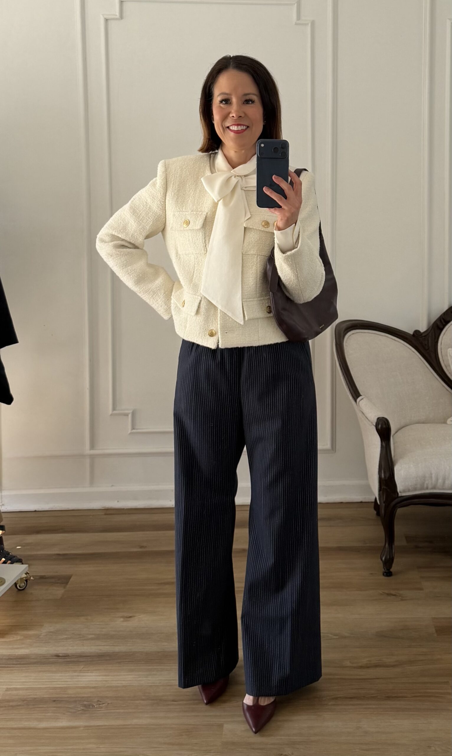 Cream tweed jacket paired with navy pinstripe wide leg trousers, a cream bow blouse, burgundy pointed toe heels, and a dark brown shoulder bag — polished spring style