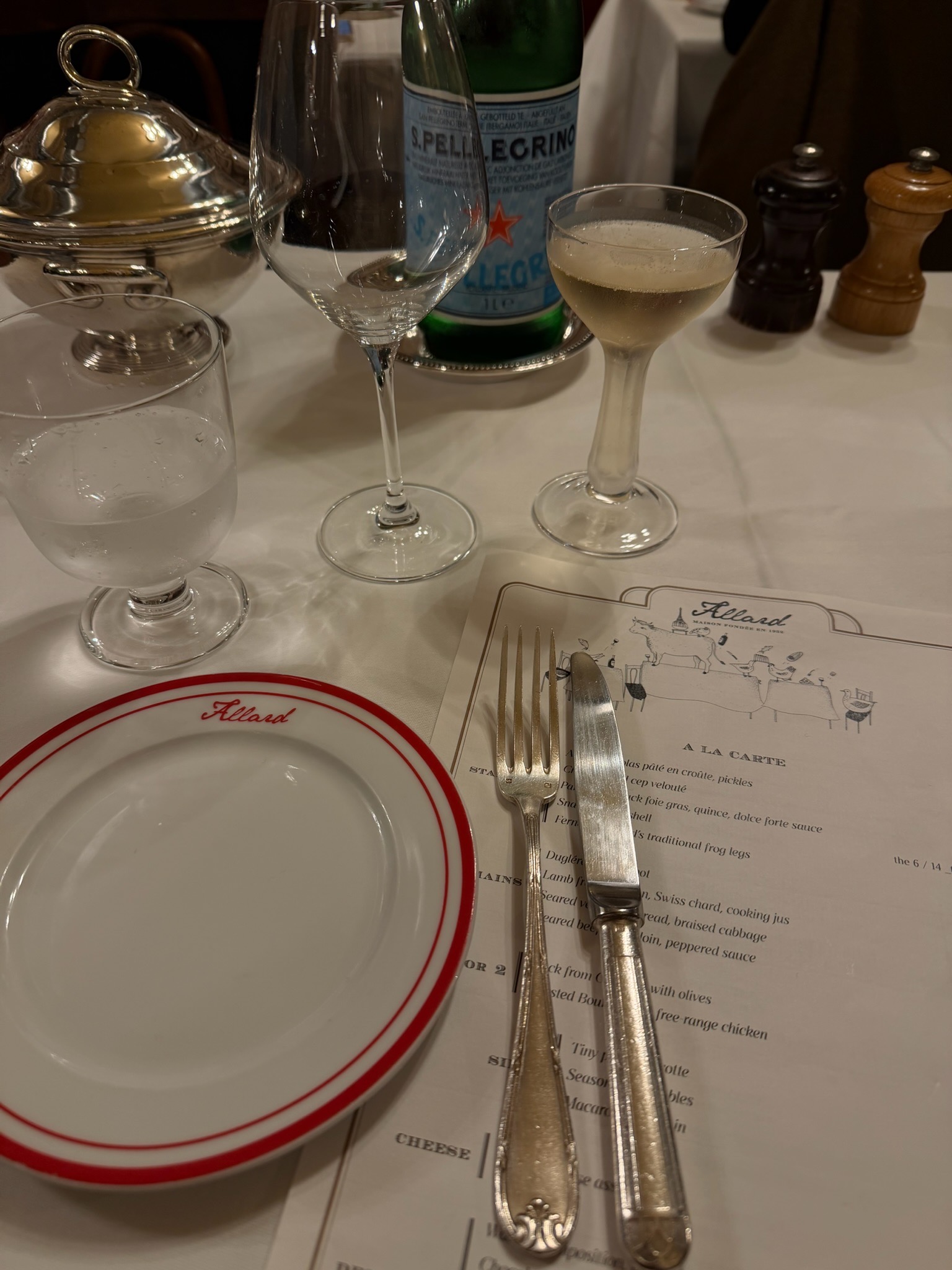 Elegant table setting at Restaurant Allard in Paris with white linen, silver cutlery, coupe glass, and à la carte menu