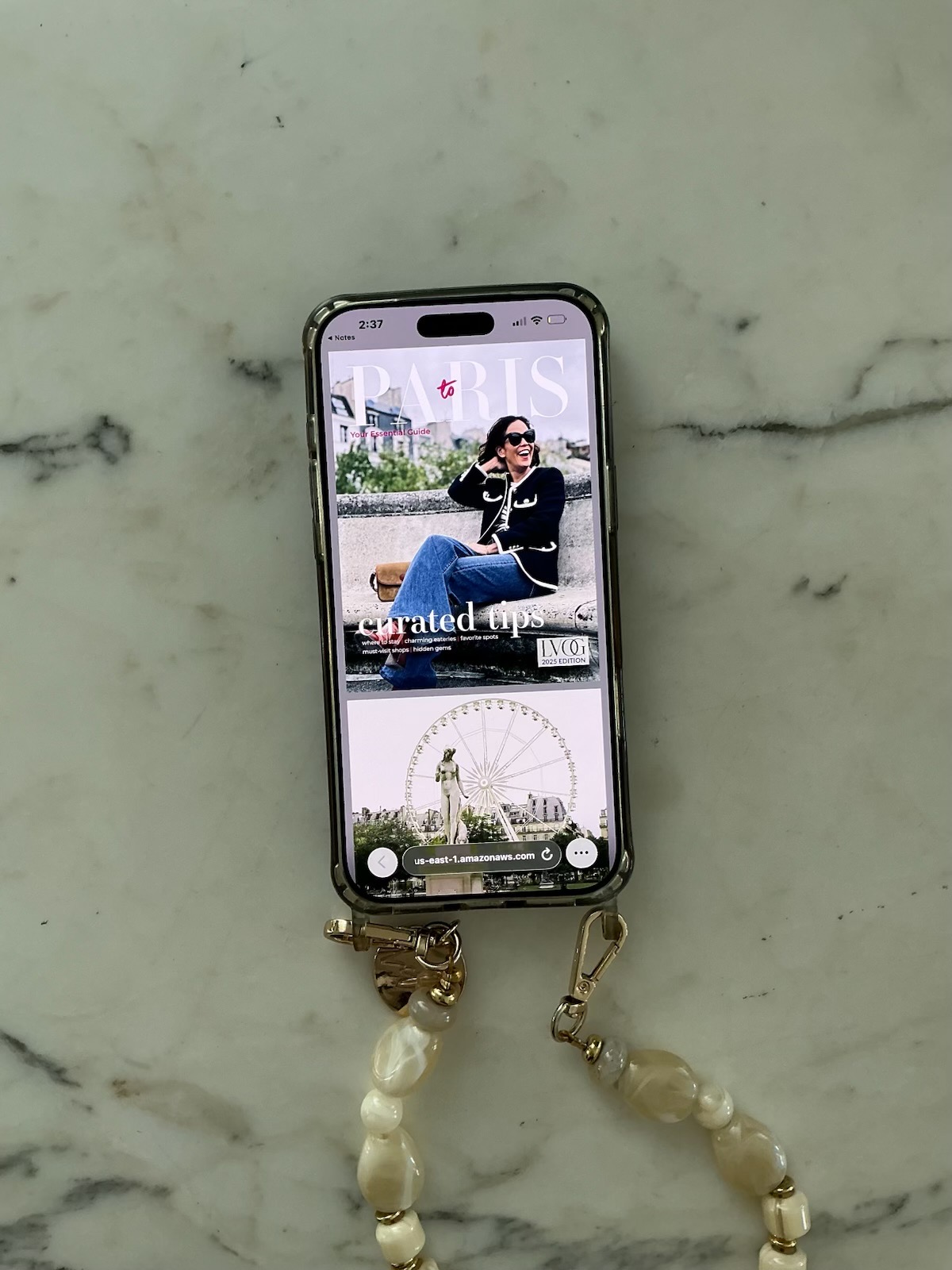 Your Essential Guide to Paris digital travel guide displayed on iPhone with pearl phone strap on marble surface