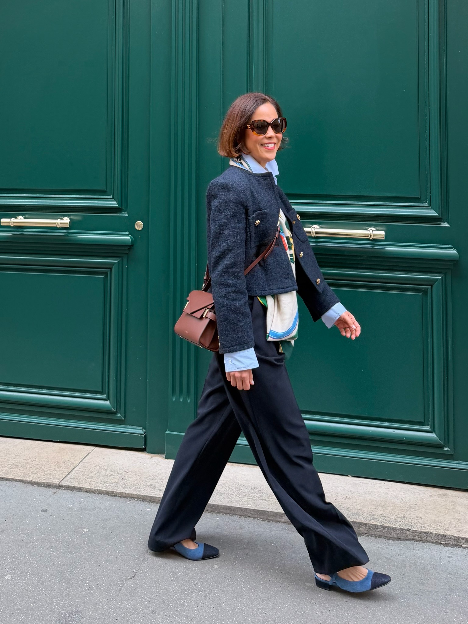 Woman in navy tweed blazer with structured crossbody bag in front of green Parisian door — elevated bag French capsule wardrobe