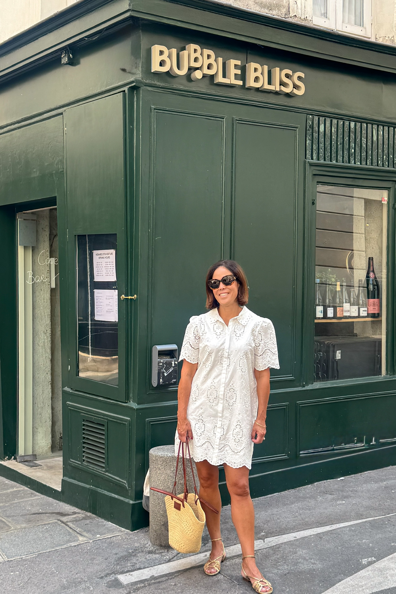 What to wear in Paris in July — white eyelet dress with wicker tote and gold sandals on a Paris street