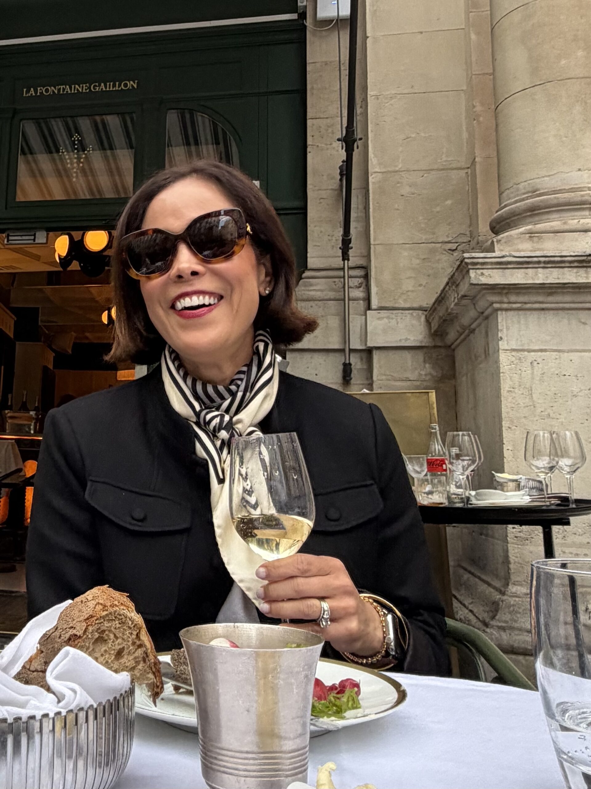 Lady wearing a stripe silk scarf holding a glass of wine at a French restaurant.