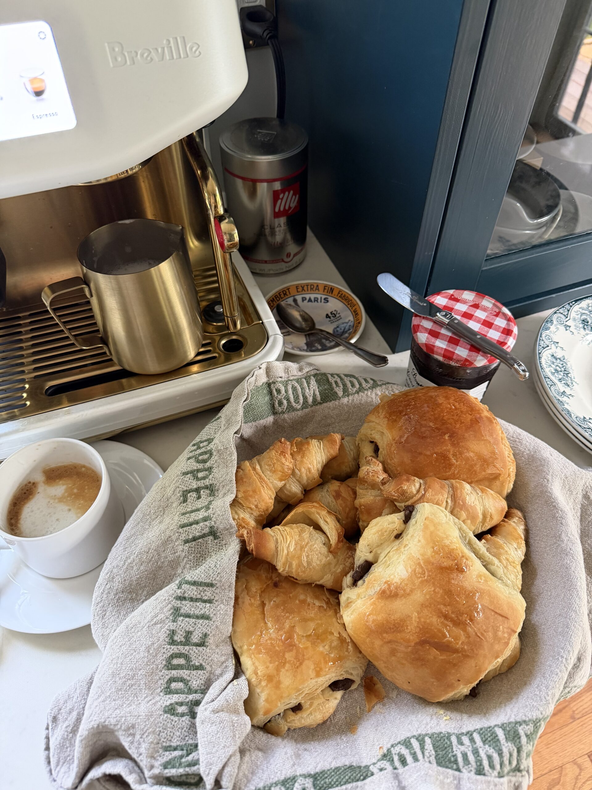 Coffee and croissant sitting on a counter with jam.